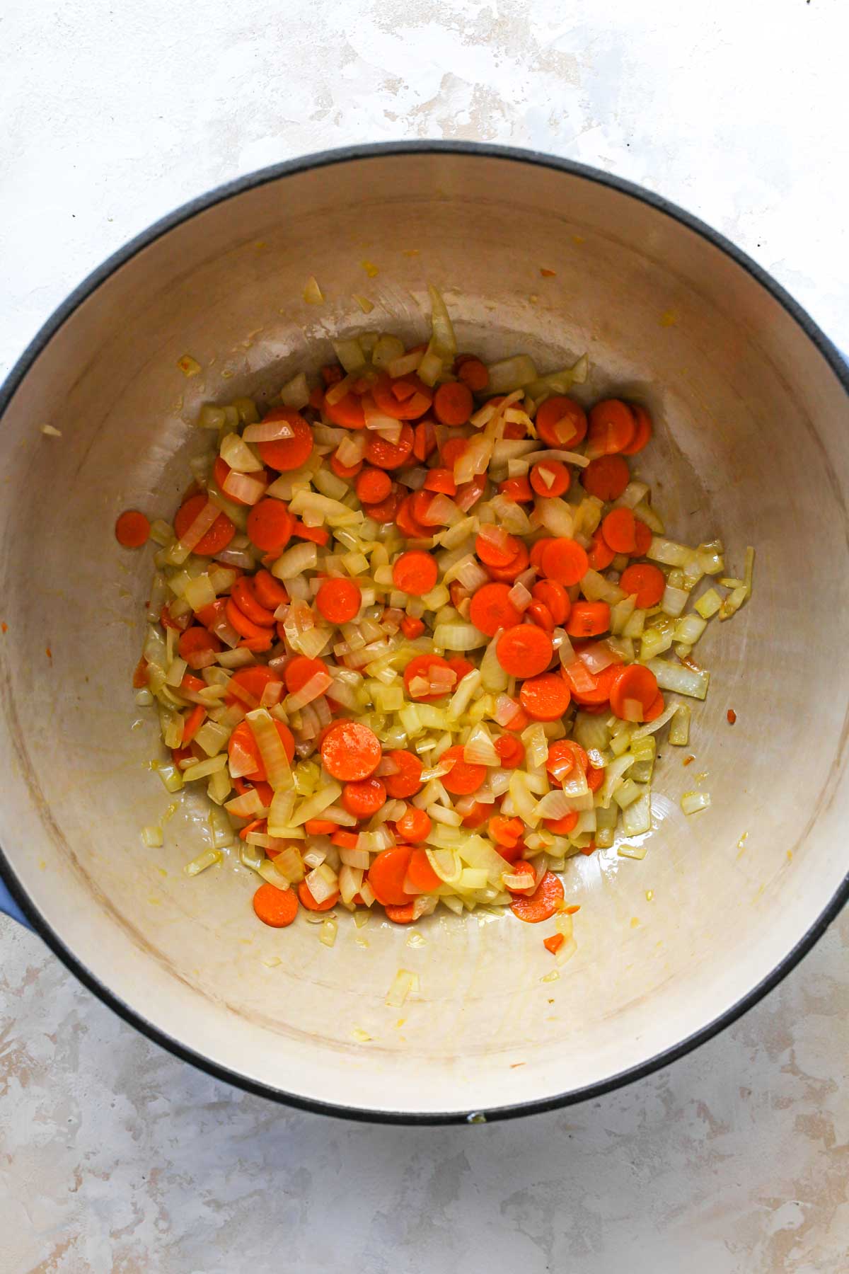 Carrots, onion, and garlic being sautéed in a Dutch oven
