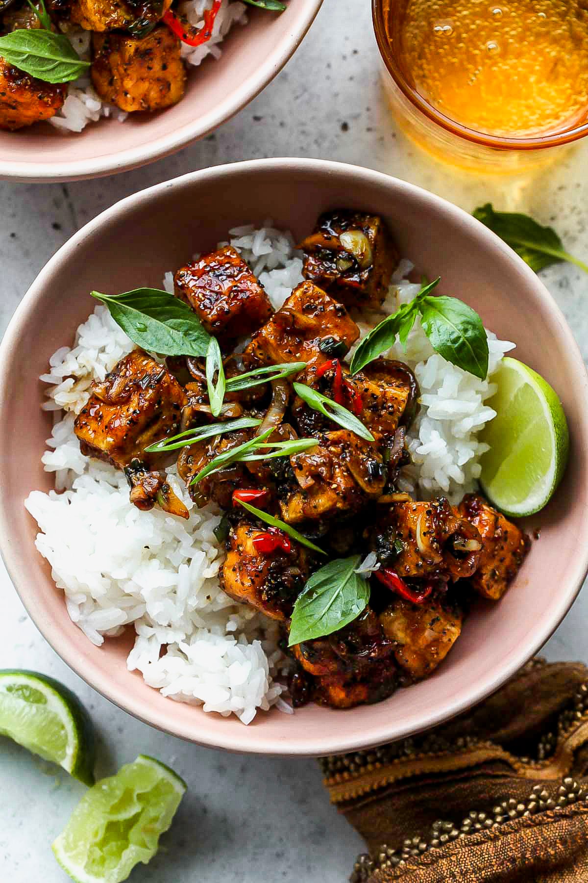Black Pepper Tofu Cubes of black pepper tofu arranged over white rice in a pink bowl with lime wedges.