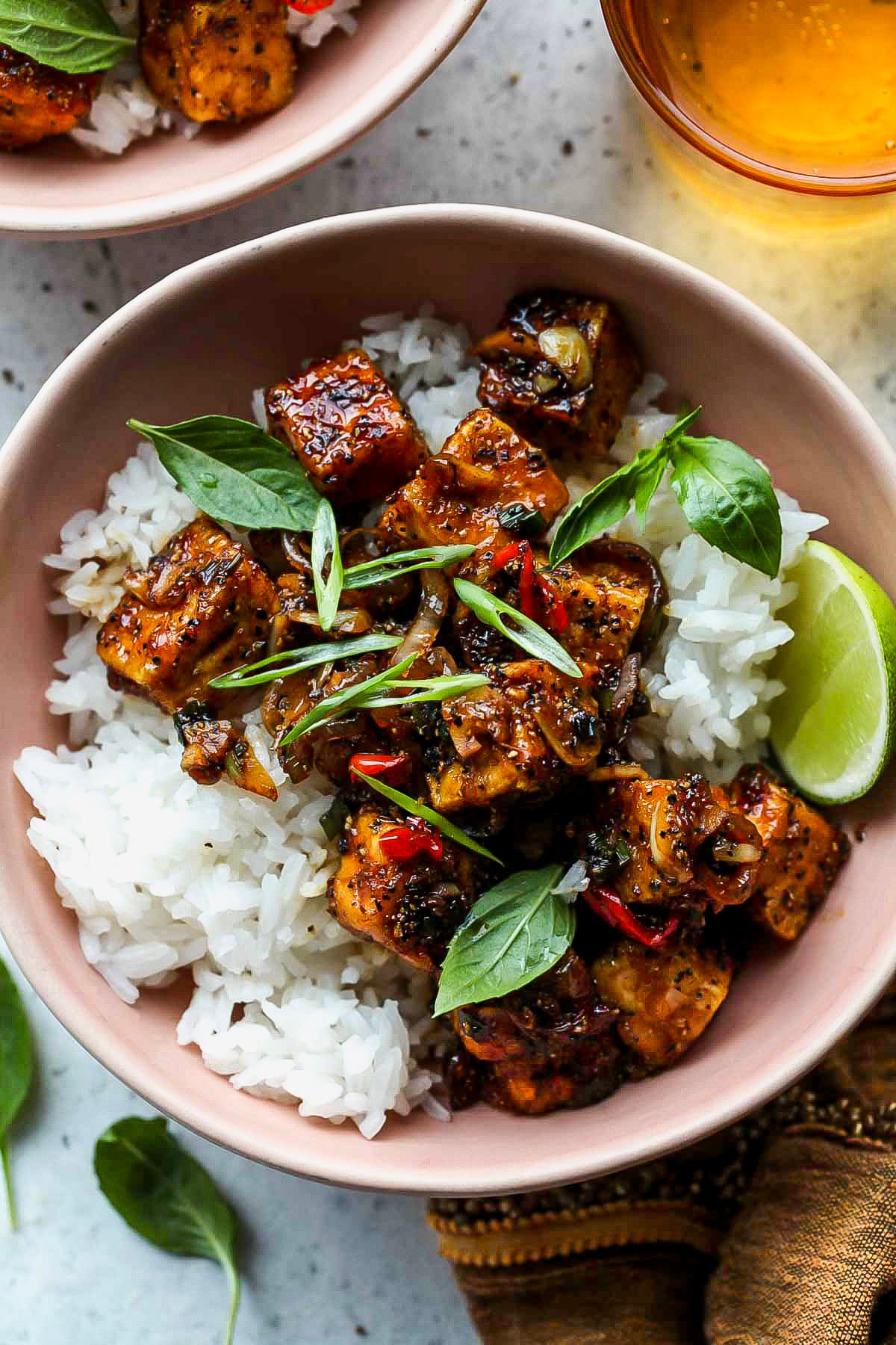 Black Pepper Tofu Black pepper tofu spooned over white rice in a pink bowl garnished with basil leaves.
