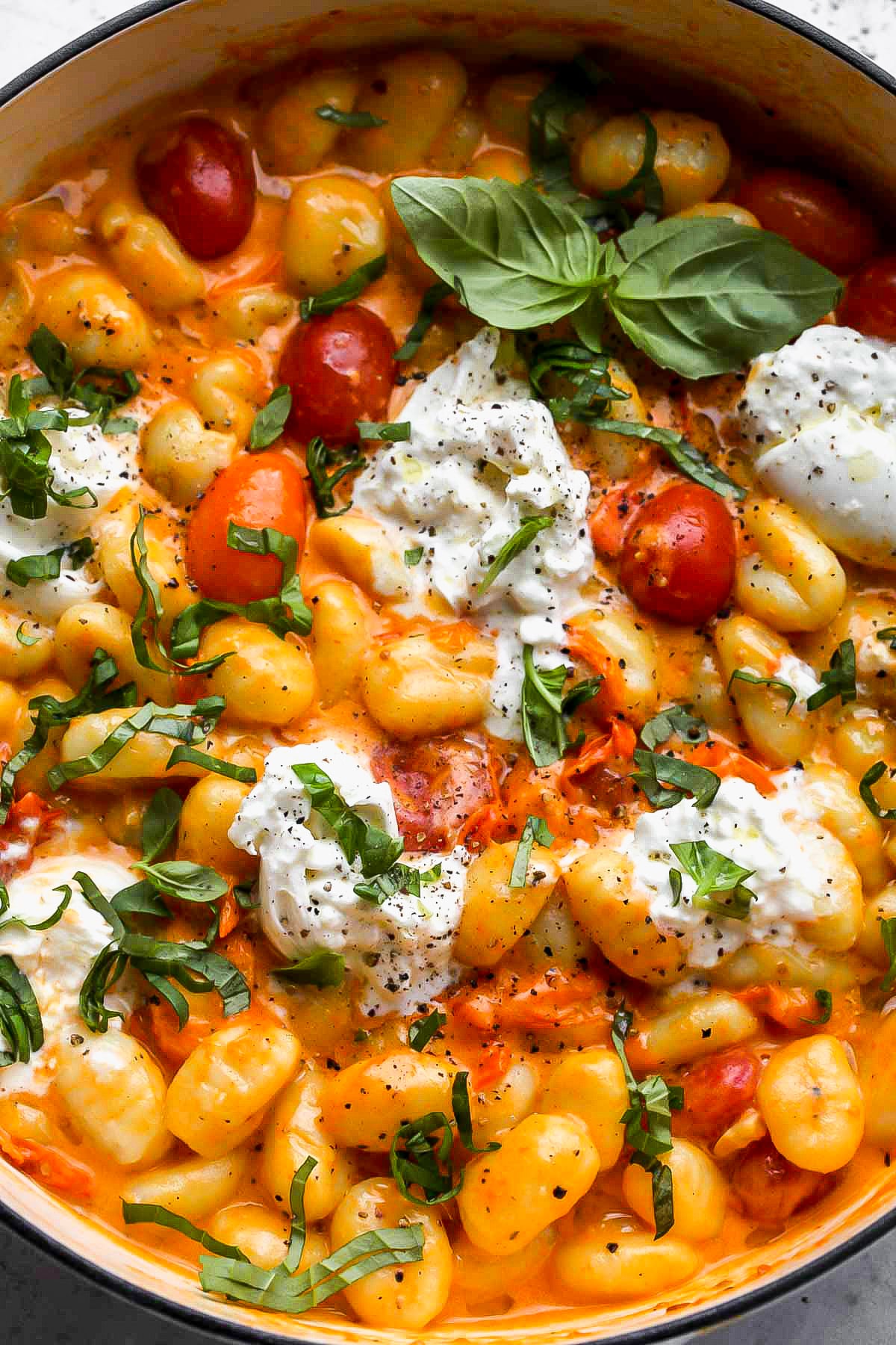 Dollops of burrata cheese and fresh basil being added to pot of pasta.
