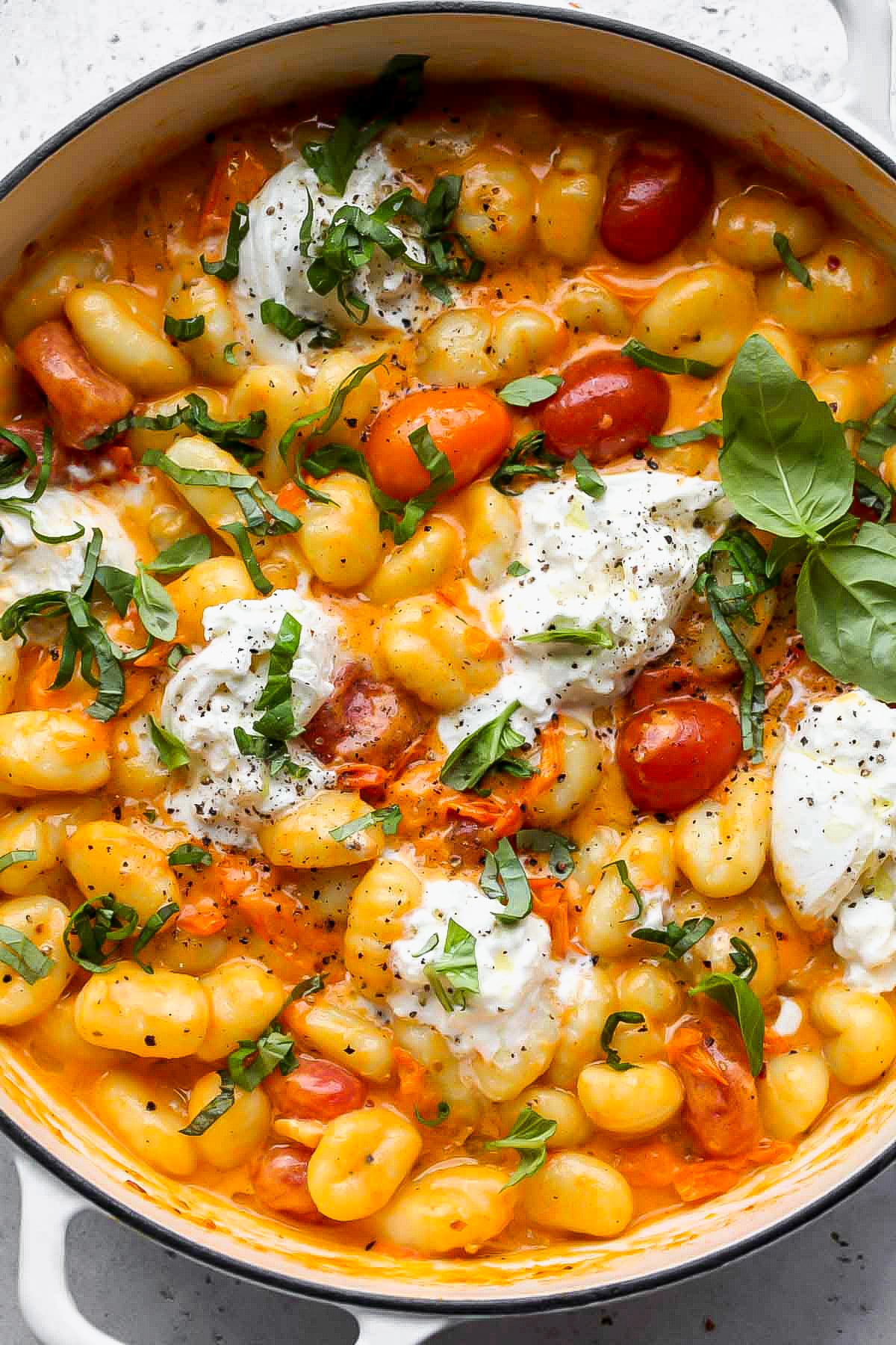 Creamy tomato gnocchi in a white pan topped with basil leaves and burrata.