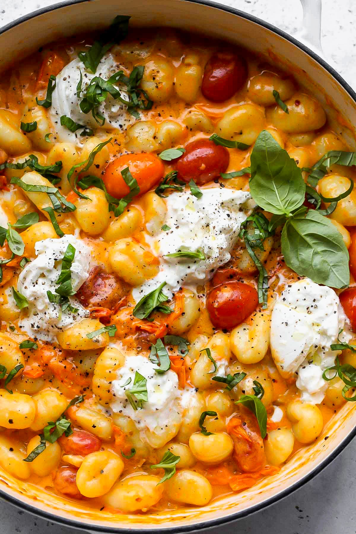 A white pan filled with tomato gnocchi recipe and garnished with fresh basil leaves, cheese, and black pepper.