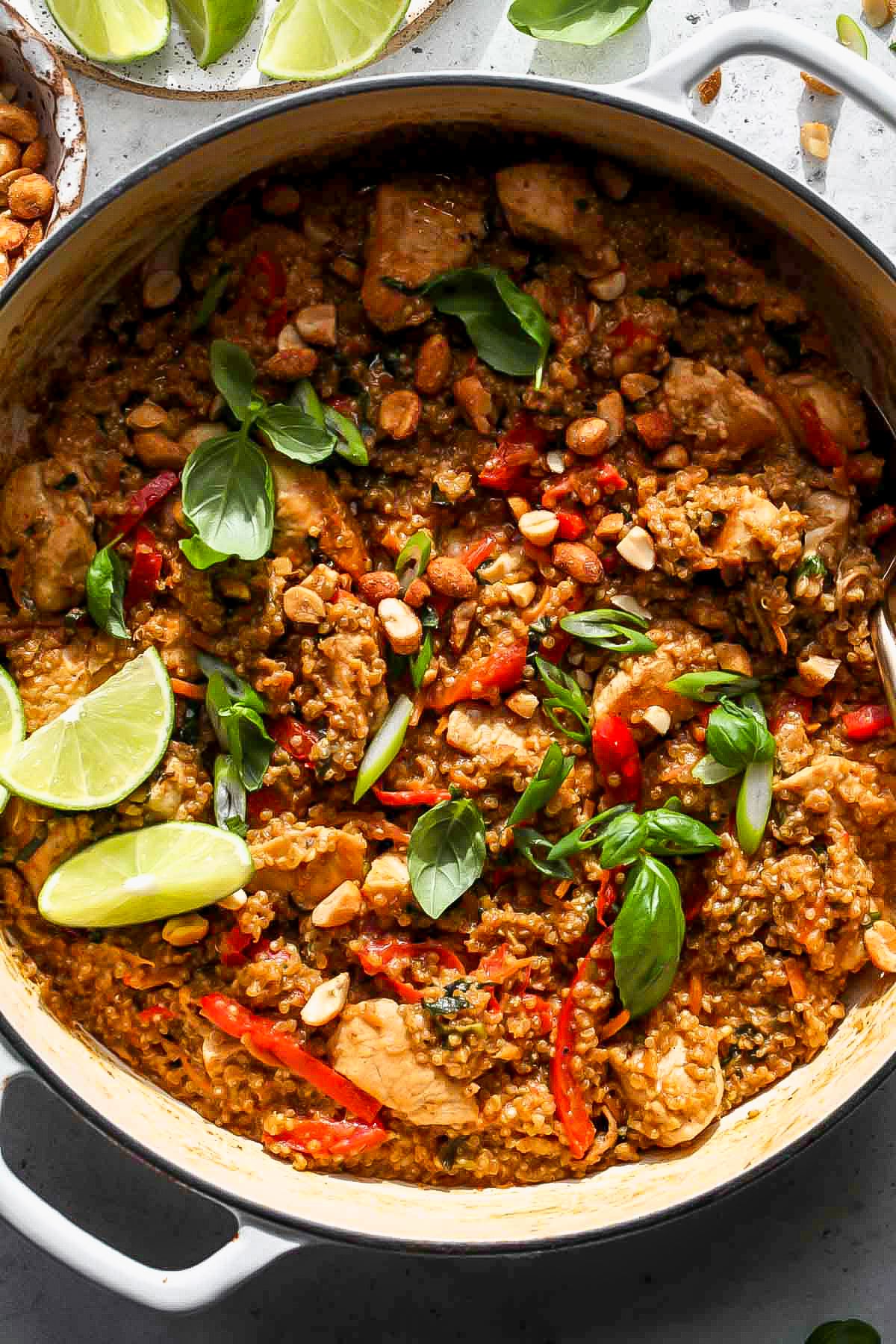 Thai peanut chicken and quinoa in a white skillet topped with basil leaves and scallions