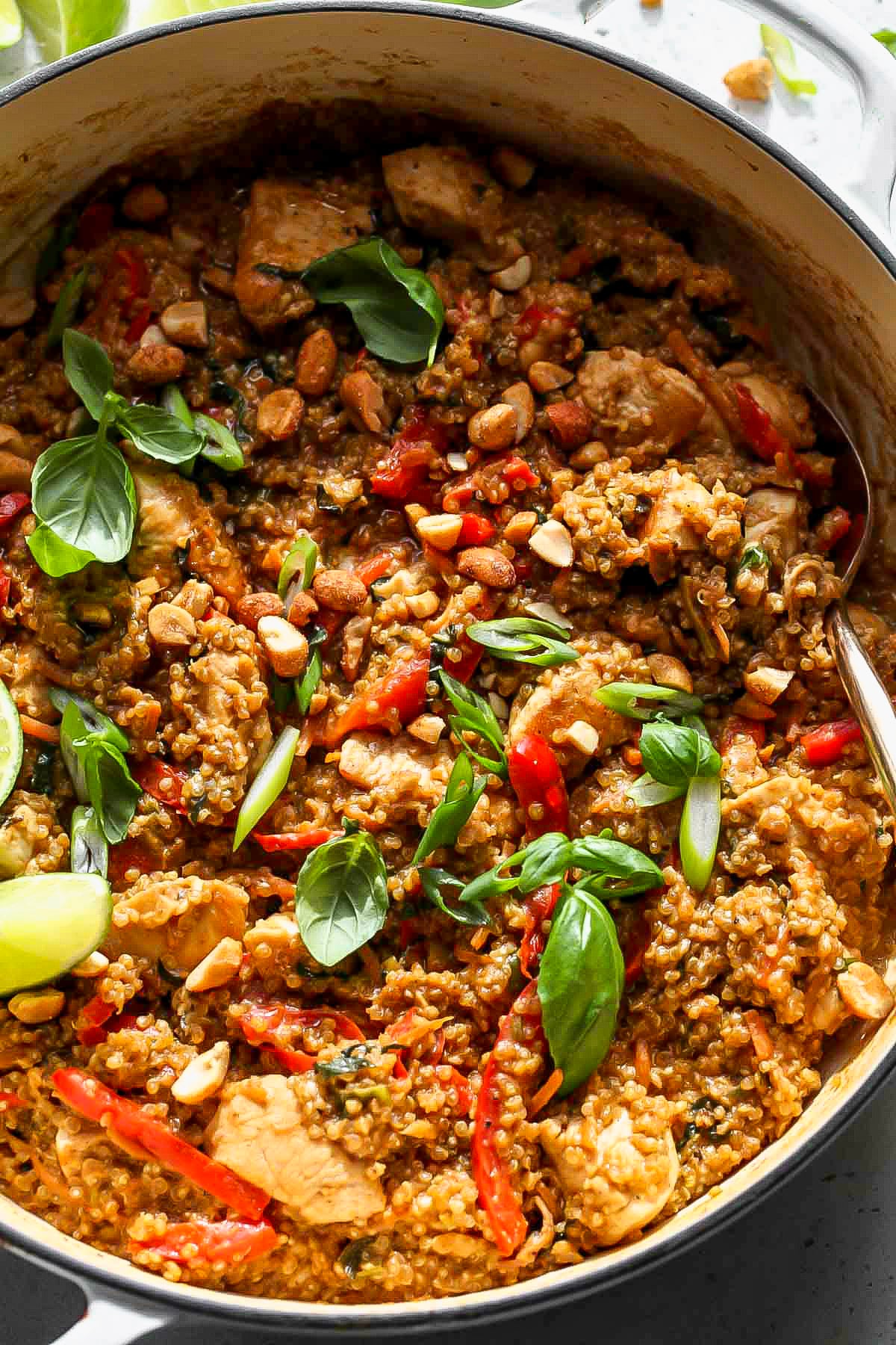 Thai chicken and quinoa in a white pan topped with lime wedges and basil leaves