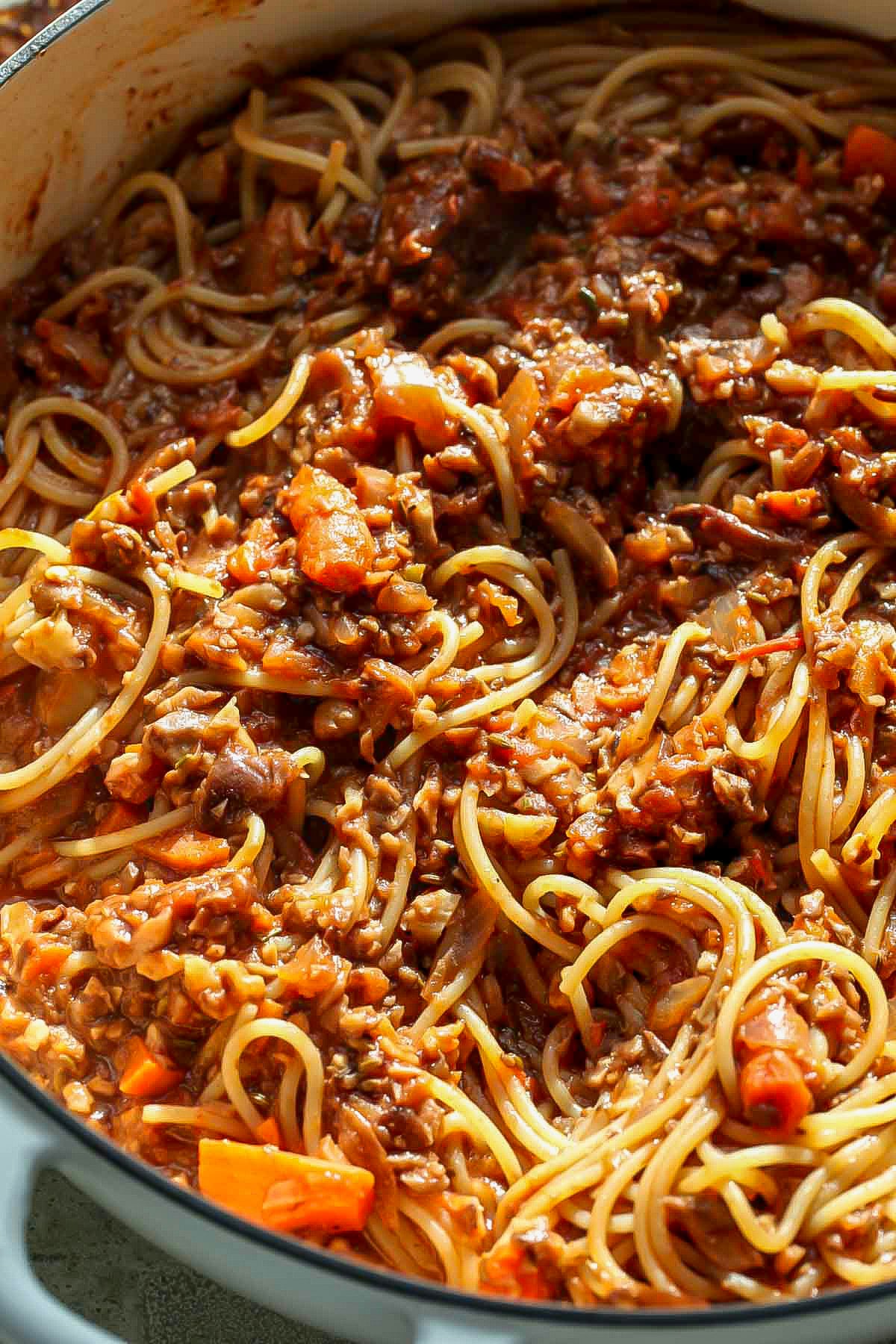 Spaghetti being tossed with bolognese sauce in a sauté pan.