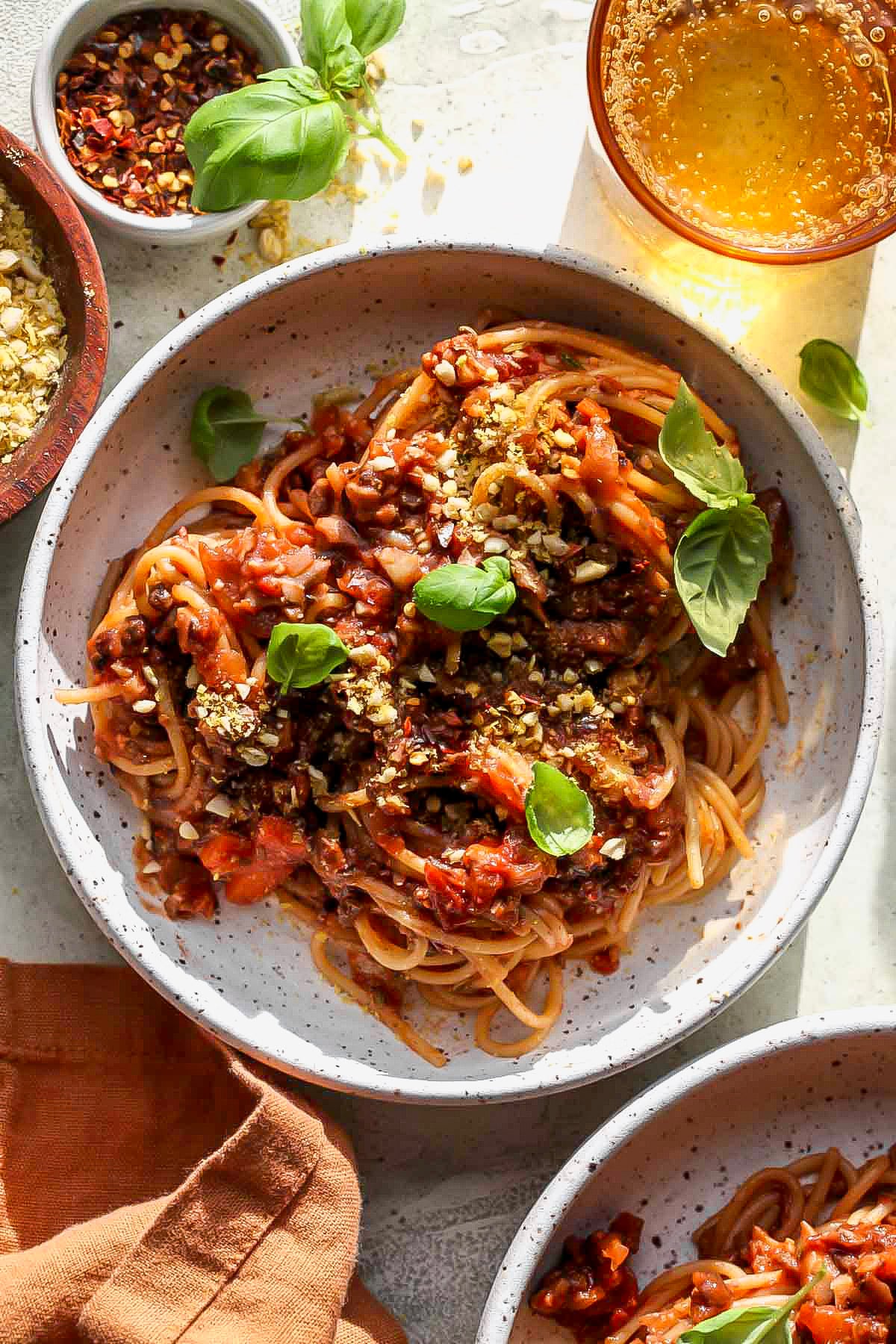 A white bowl filled with vegan spaghetti bolognese topped with fresh basil.