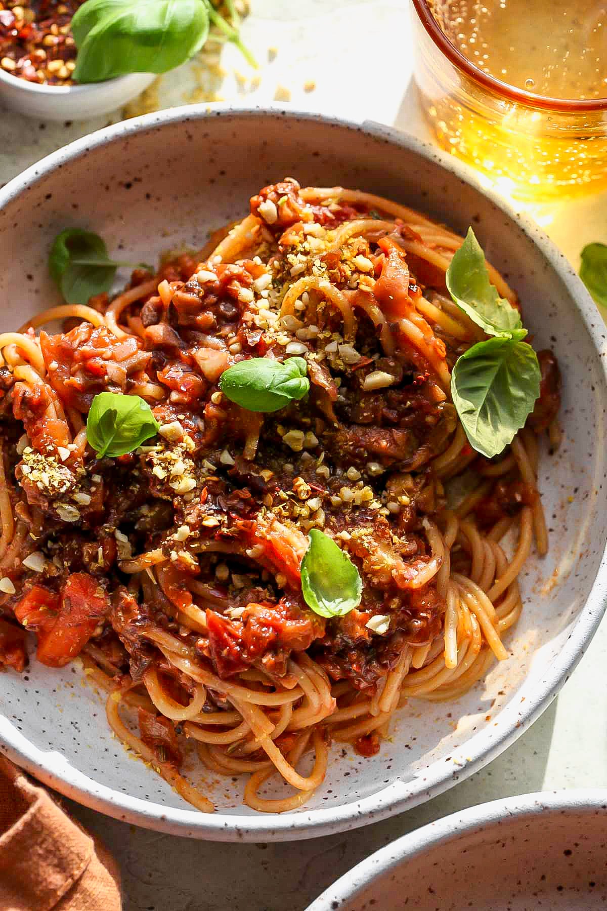 A white plate filled with a portion of vegan bolognese topped with fresh basil leaves.