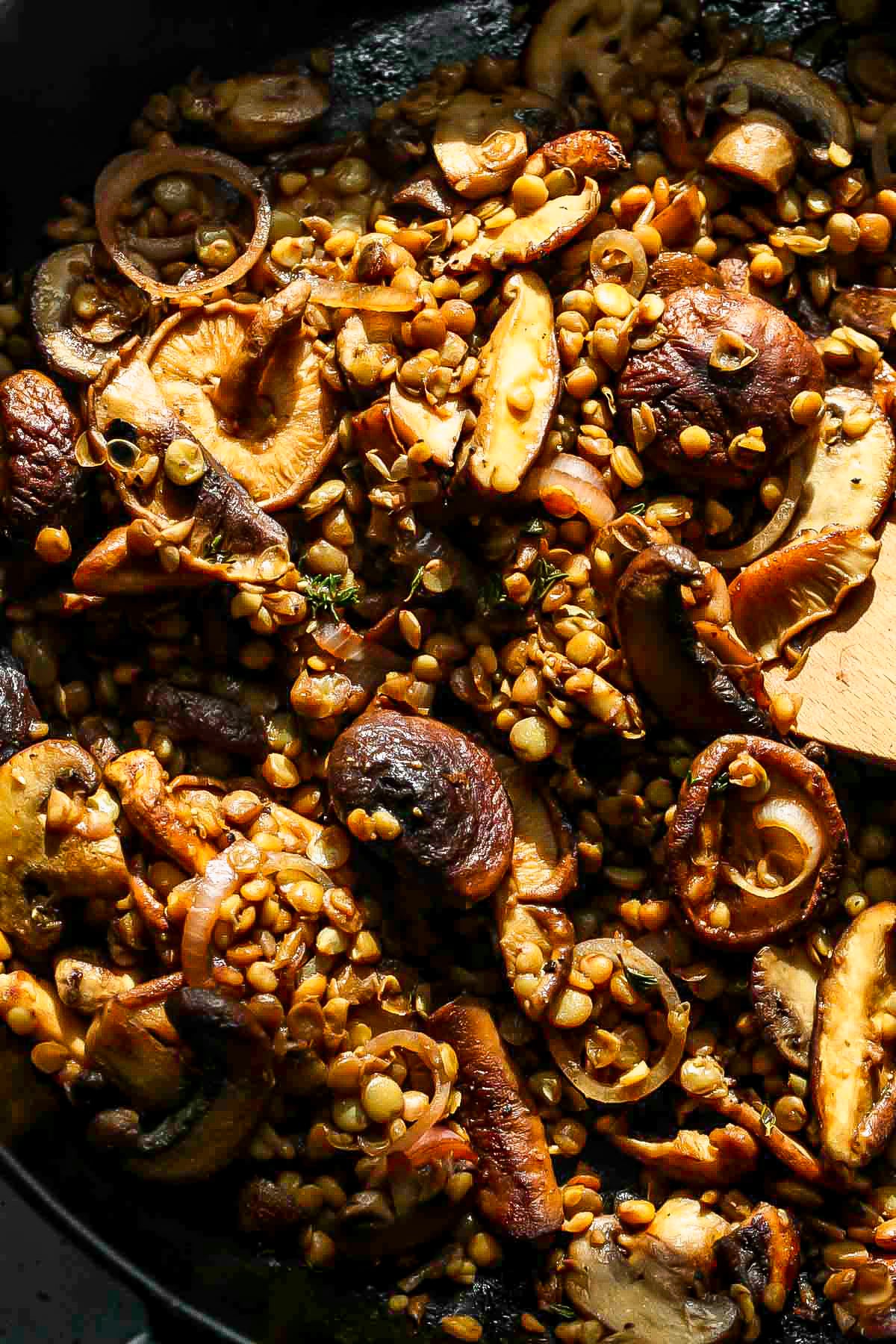 Balsamic mushrooms and lentils being mixed in a black skillet.