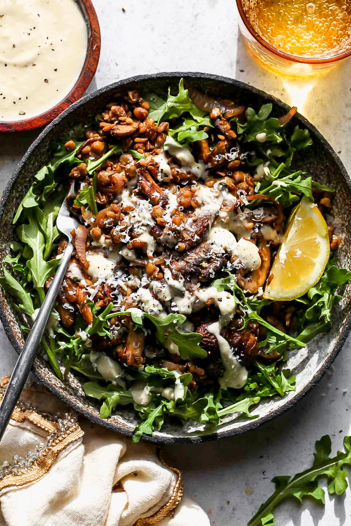 Warm lentil salad served over arugula in a grey bowl.