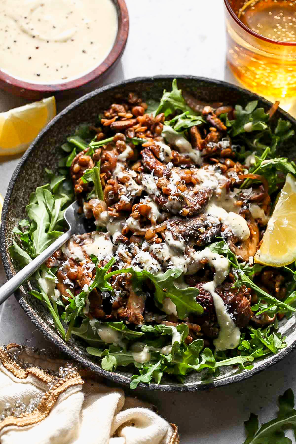 Warm balsamic and lentil mixture being served over arugula and topped with garlic dressing.