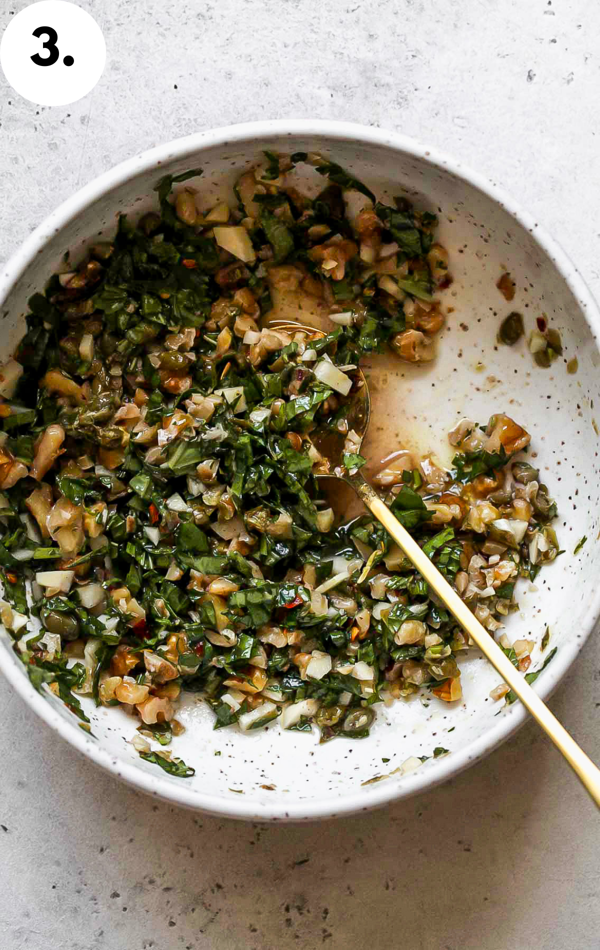 Garlic-herb mixture being combined in a white speckled bowl.