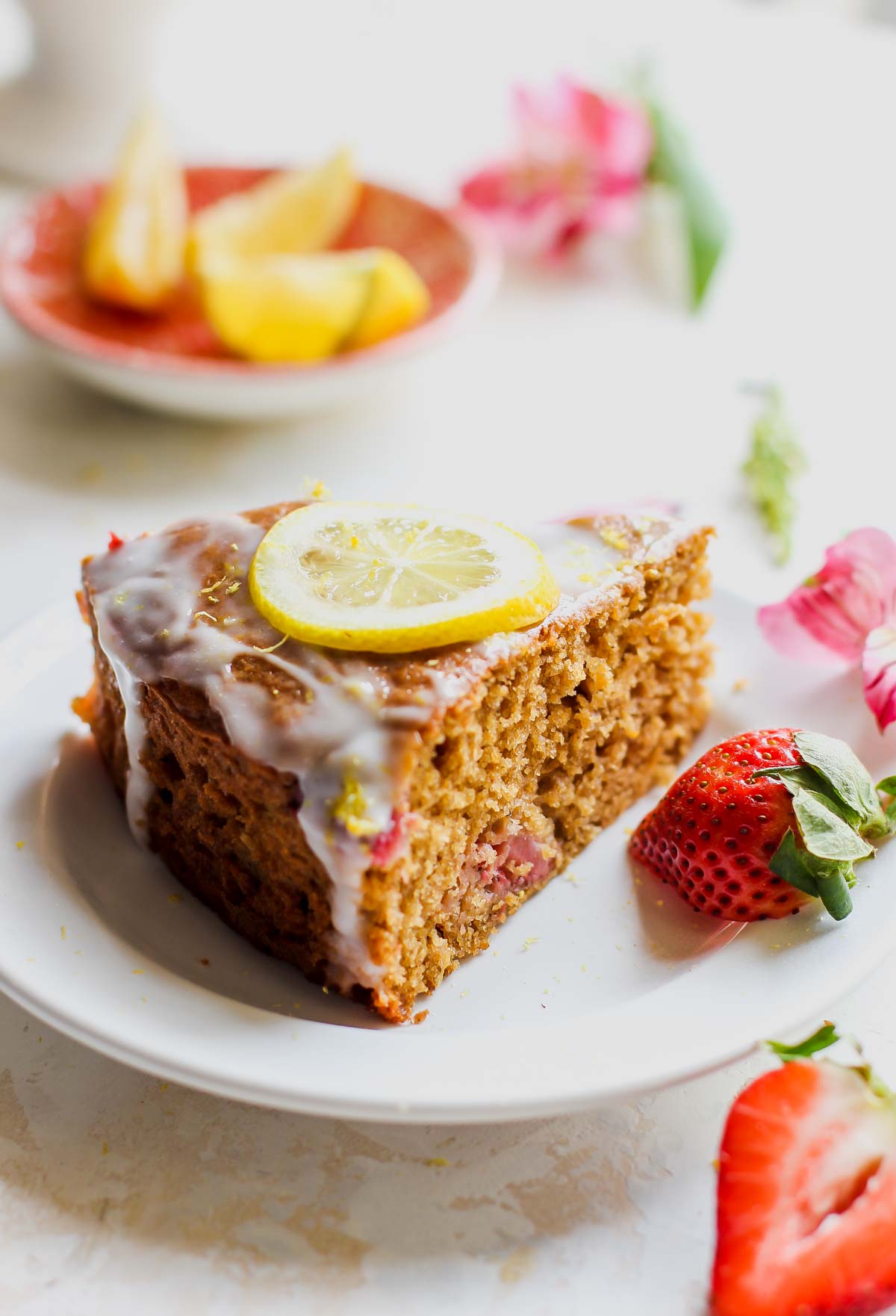 Slice of brunch cake on a white plate with a strawberry resting on the side.