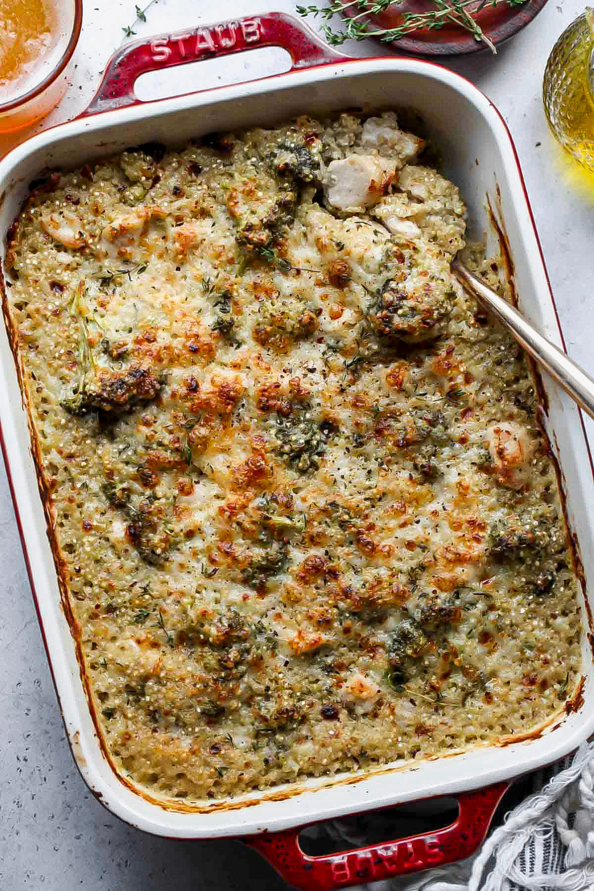 Chicken broccoli bake in a red baking dish with a serving spoon digging in.