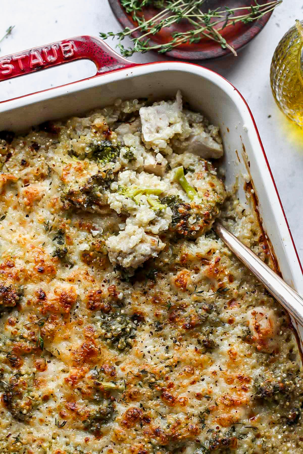 A spoon digging into the corner of a baking dish filled with chicken, broccoli, and quinoa mixture.