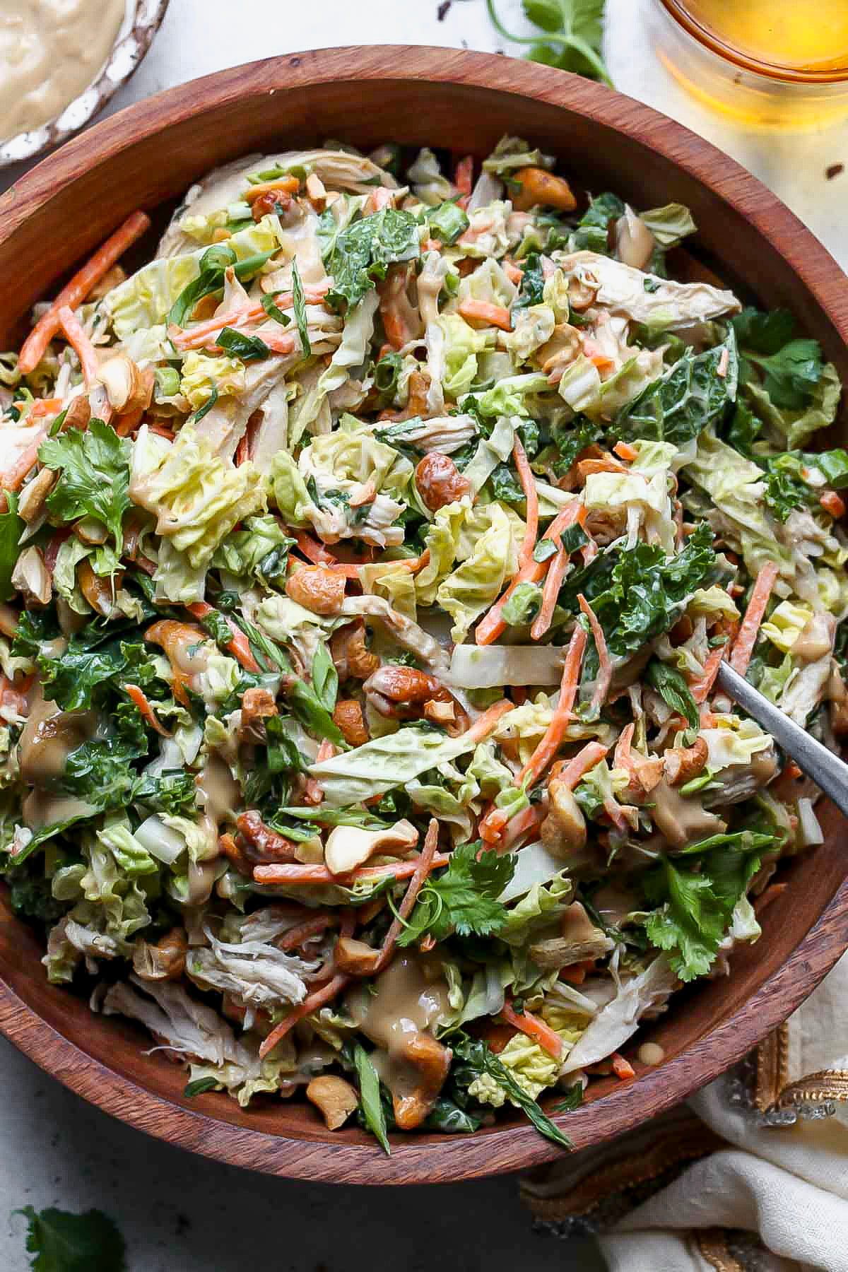 Chicken cashew crunch salad being tossed in a wooden serving bowl.