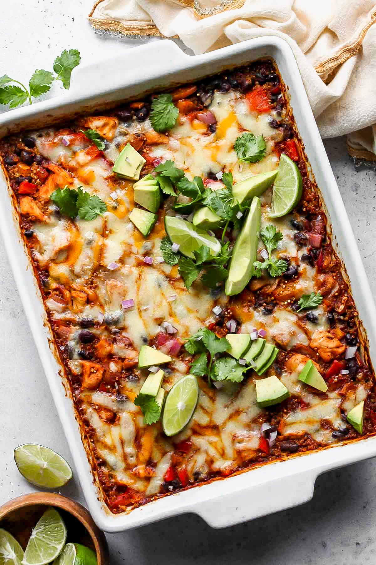 Chicken Enchilada Bake styled in a white baking dish topped with avocado and cilantro.