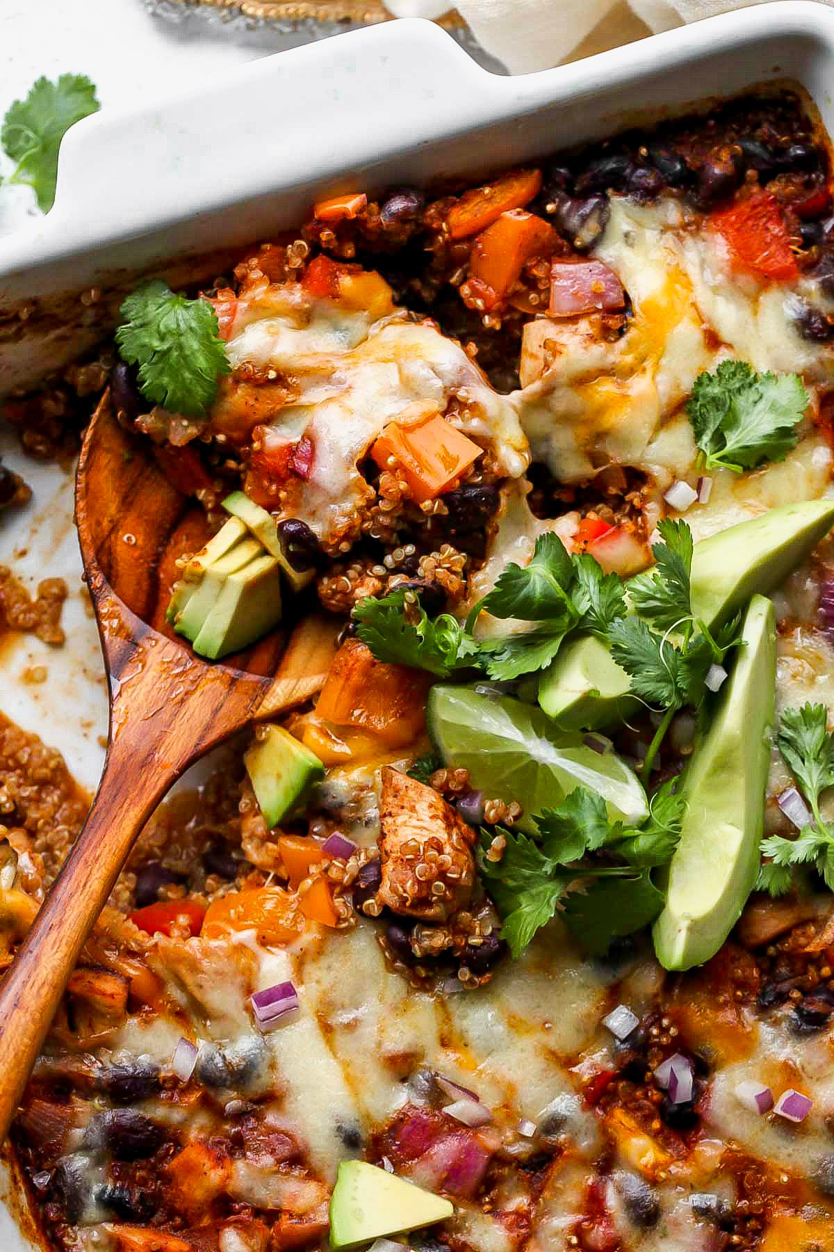 A serving spoon digging into a pan of chicken enchilada bake.