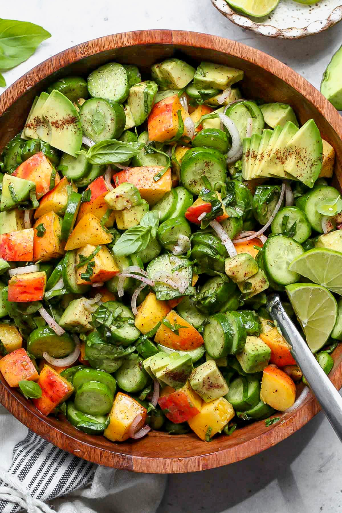 Cucumber peach salad in a large wooden serving bowl with a spoon resting on the right side.