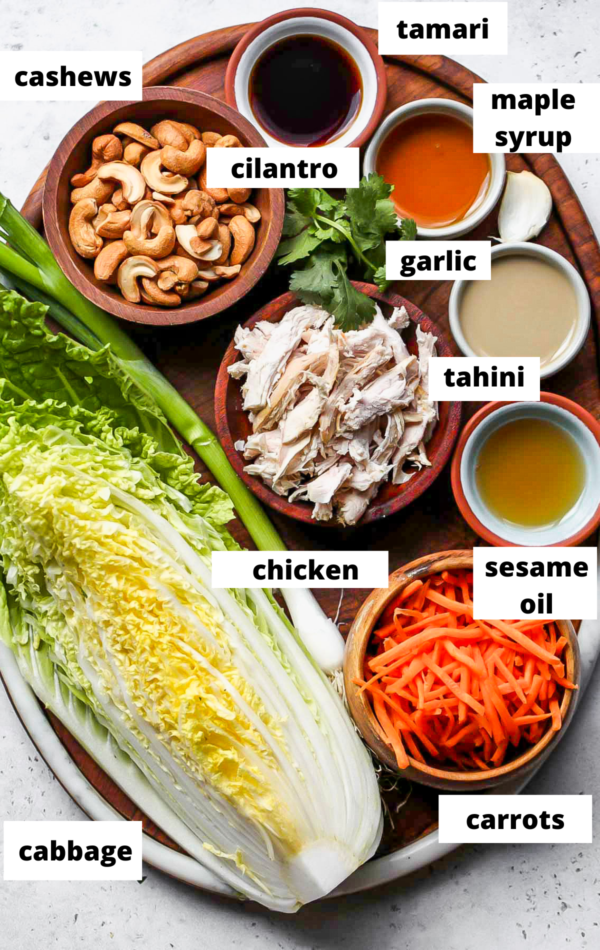Recipe ingredients in separate bowls with labels on a wooden serving board.
