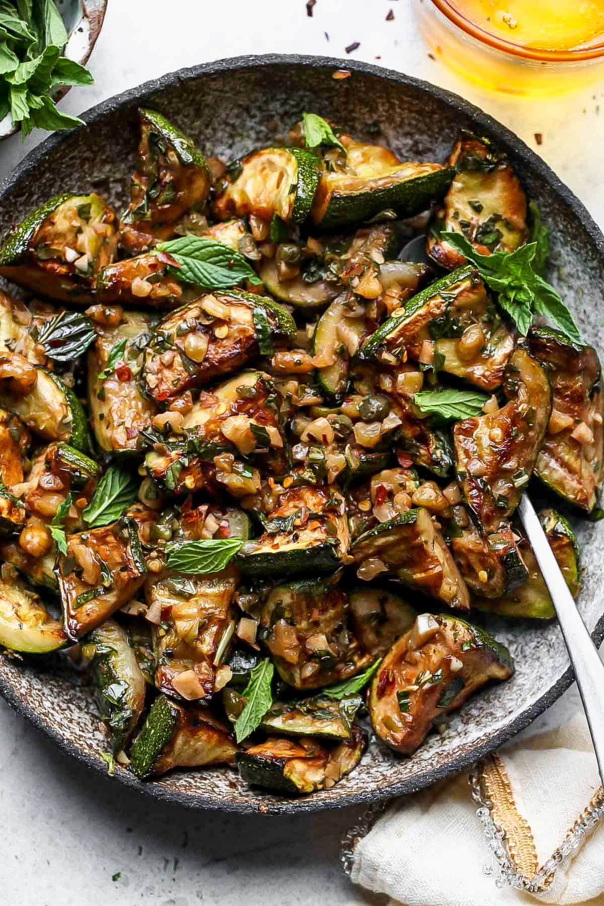 Sauteed zucchini in a grey serving bowl with a serving spoon resting on the right side.