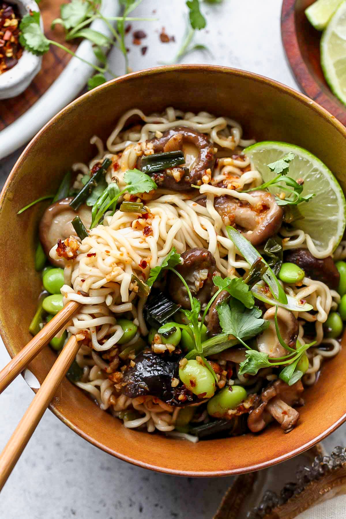 Chopsticks twirling a bite of spicy ramen noodles out of a gold bowl.