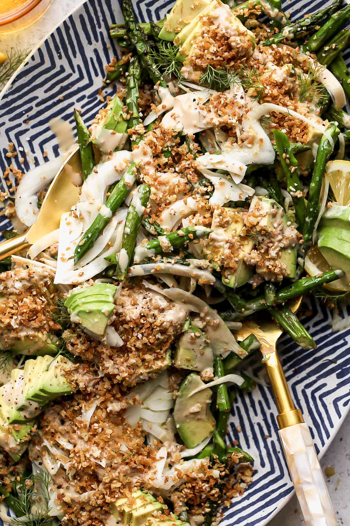 Gold salad tongs tossing asparagus and avocado salad.
