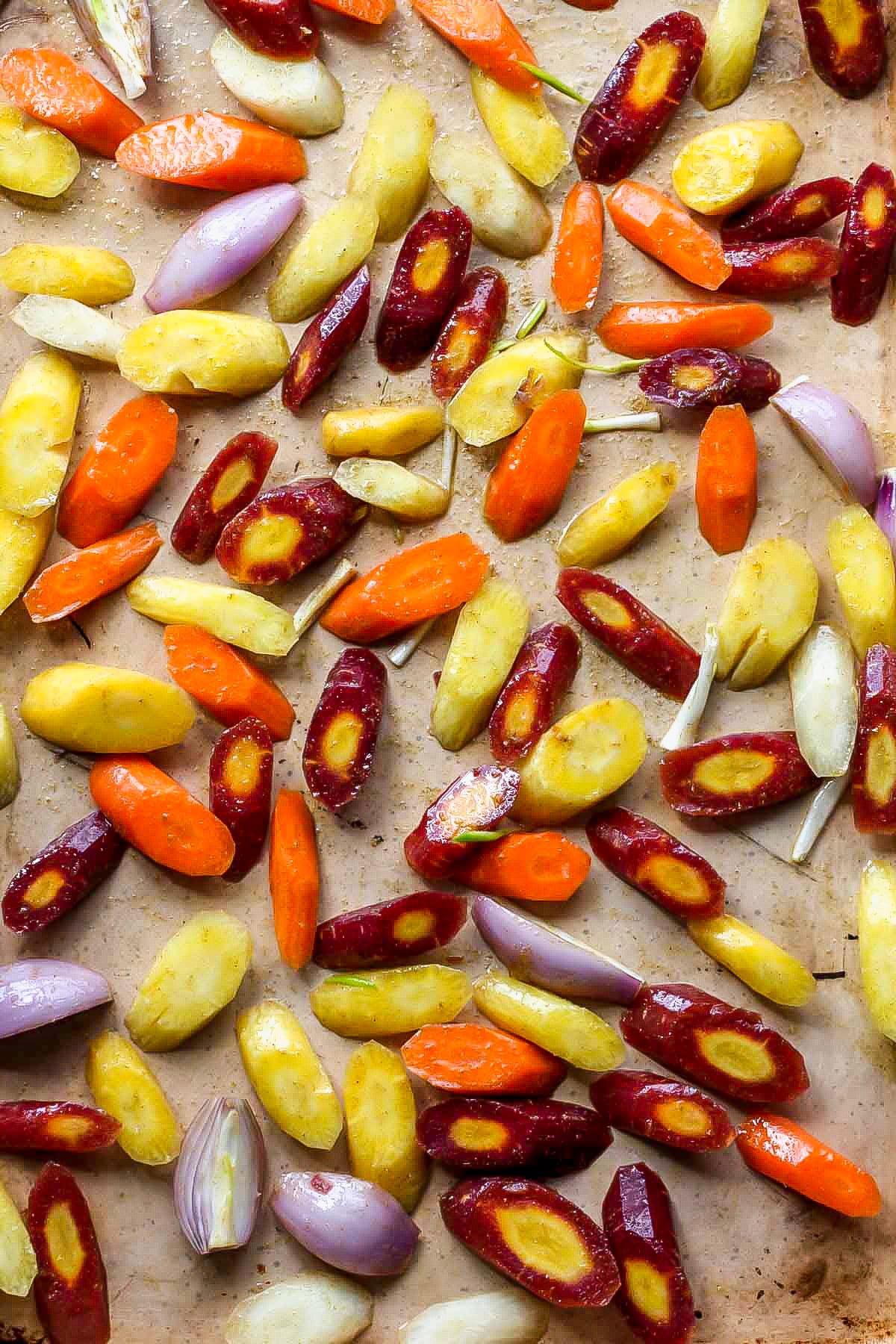 Sliced carrots and shallots tossed in olive oil and spices and arranged on a baking sheet.