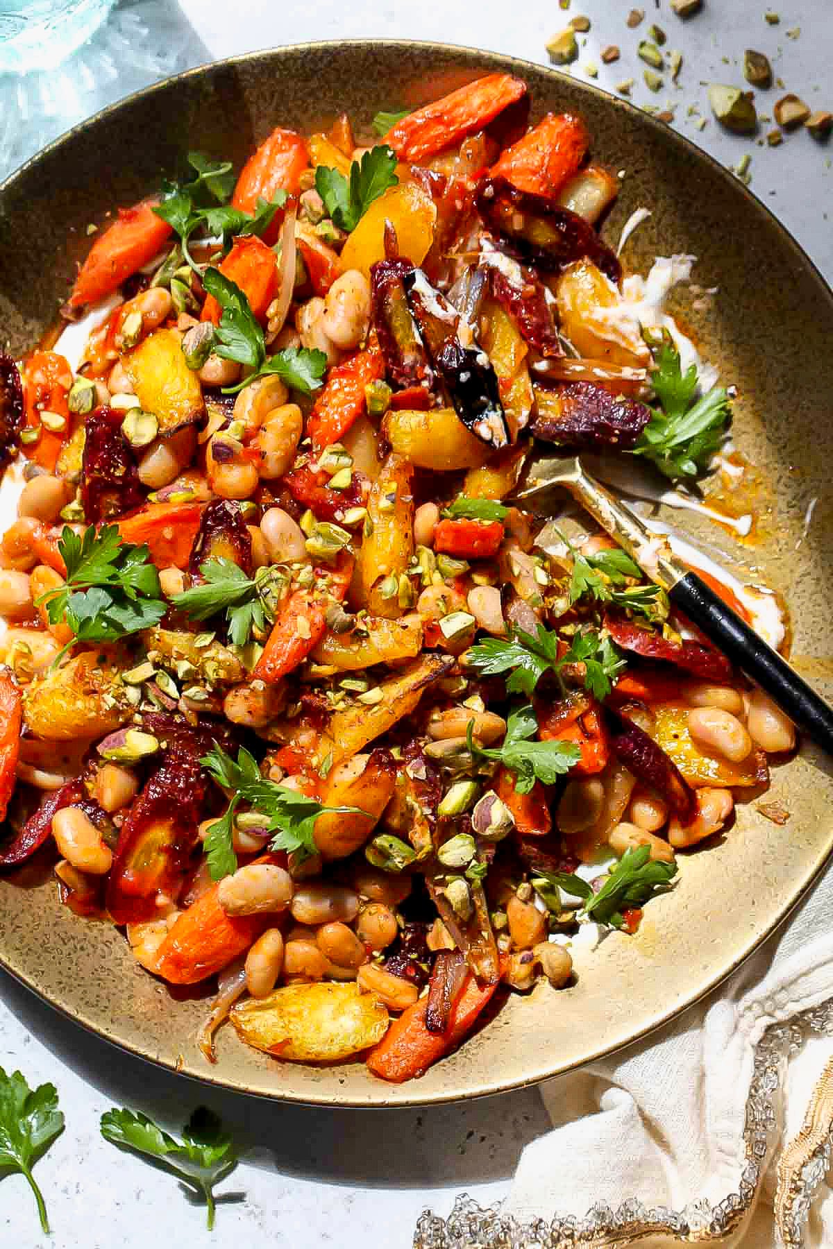 A serving spoon digging into a plate of roasted carrot salad.