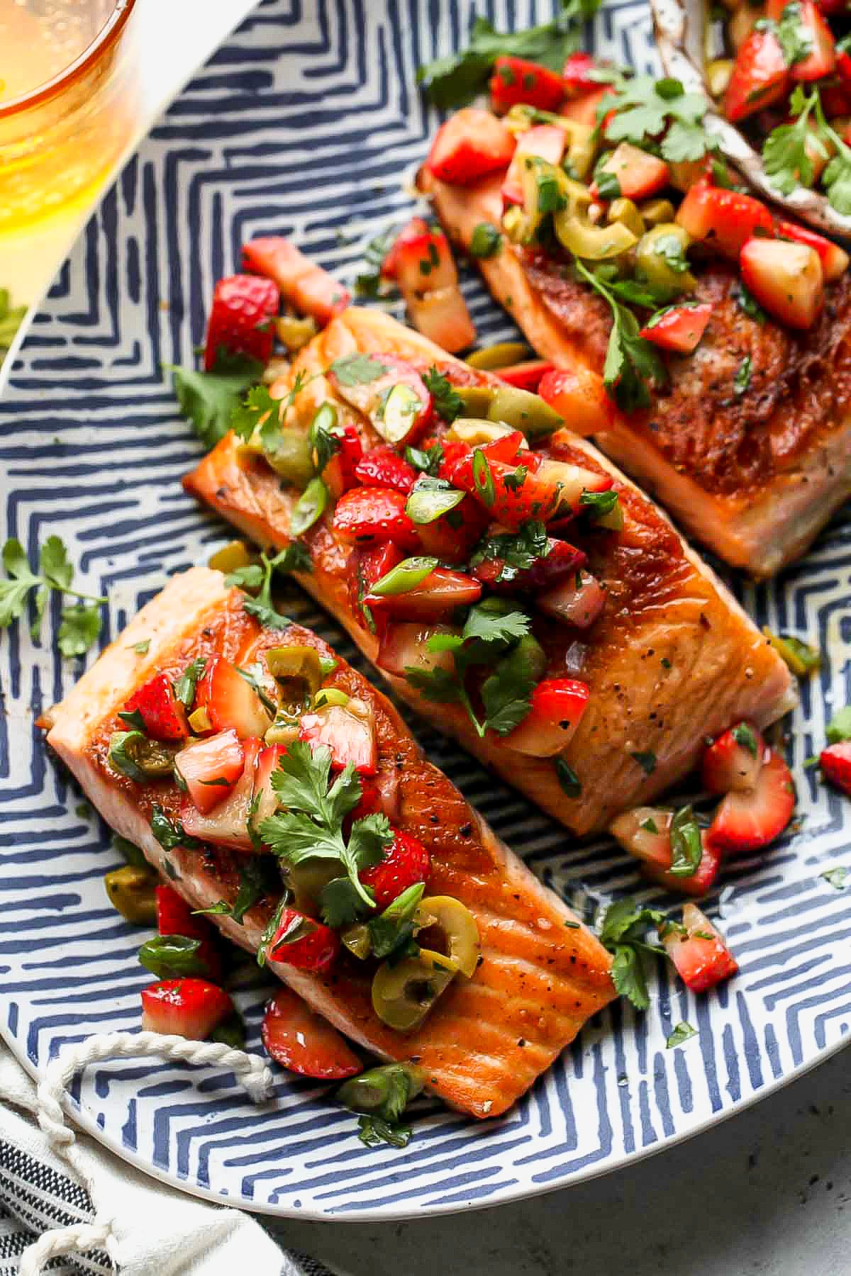 Salmon with strawberry tapenade arranged on a blue striped serving platter.