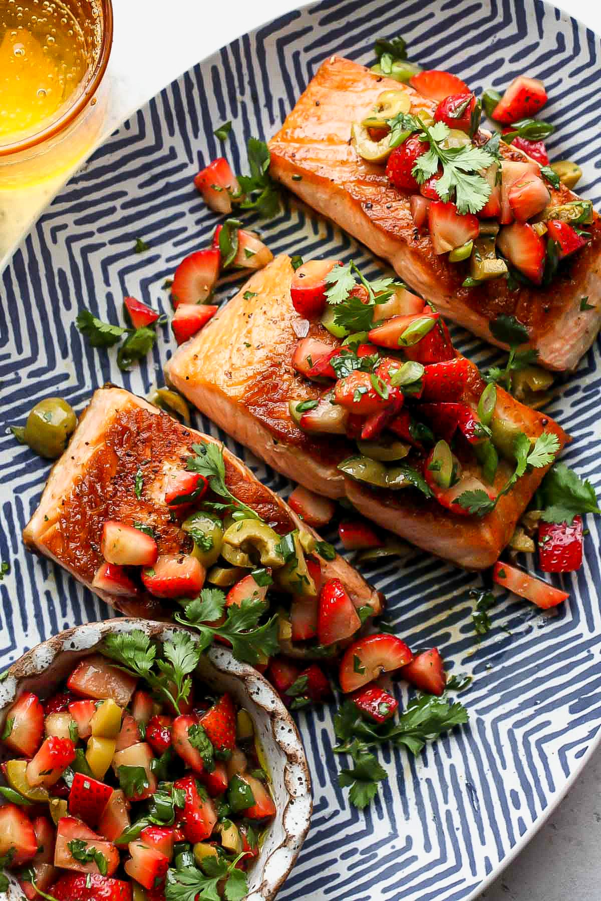 Salmon fillets arranged on a serving platter next to a bowl of strawberry tapenade.