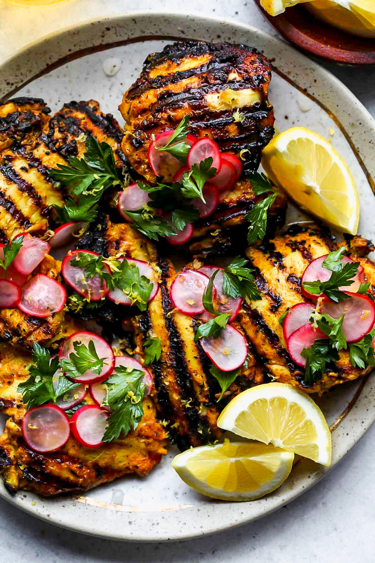 Turmeric chicken thighs on a plate with lemon wedges and radish salad as garnish.