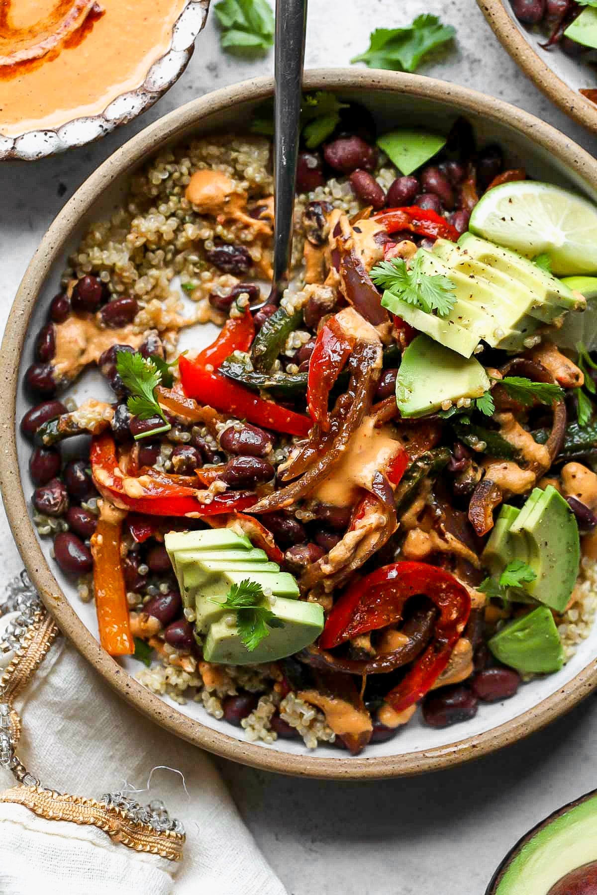 A fork digging into a plate of quinoa, black beans, peppers and onions, and avocado.
