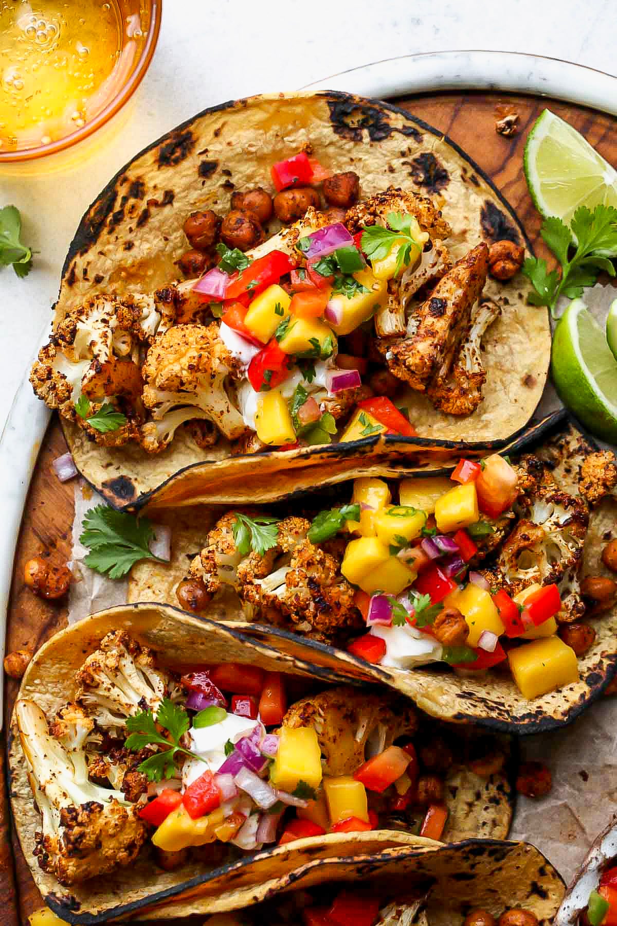 Vegan cauliflower tacos arranged on a serving platter with a bowl of mango salsa on the side.