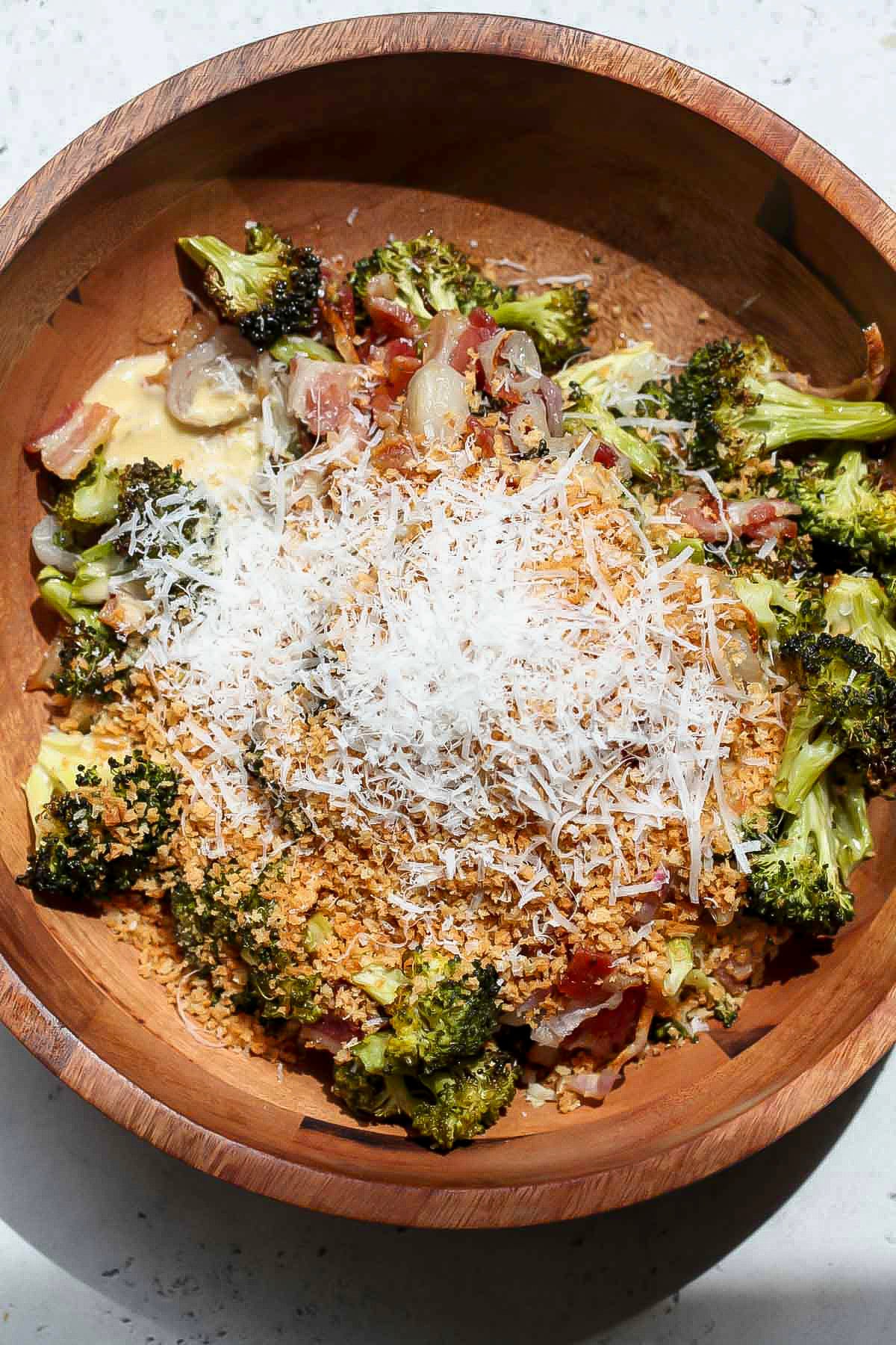 Salad being assembled in a wooden bowl, topped with Miso-Caesar dressing, panko, and cheese.