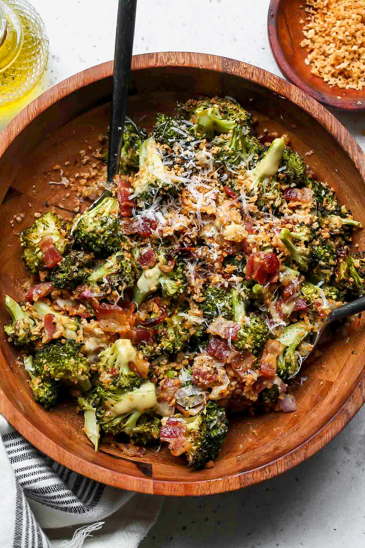 Roasted broccoli salad in a wooden serving bowl with serving utensils resting on each side.