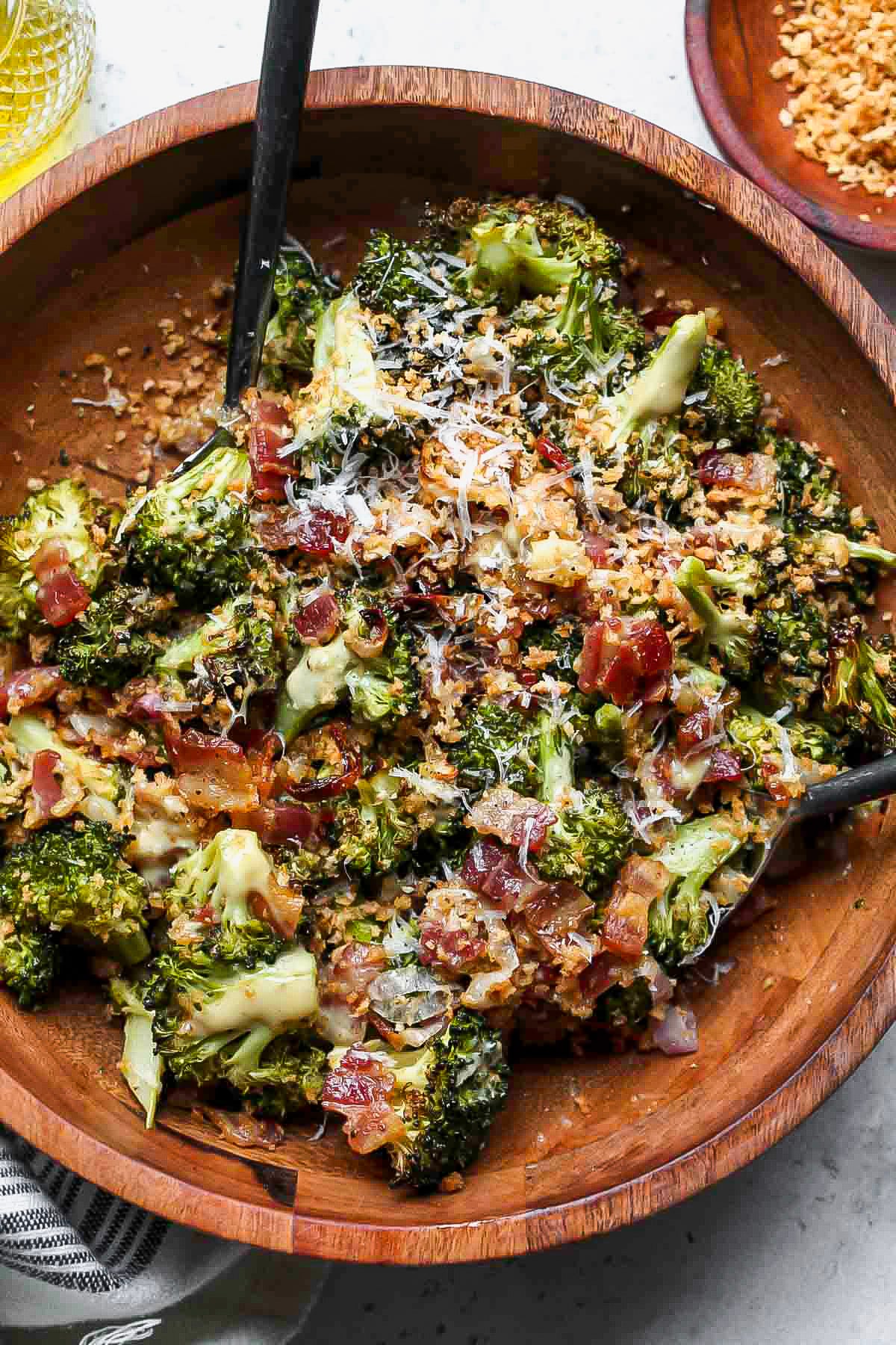 Serving utensils tossing Roasted Broccoli Salad in a large wooden serving bowl.