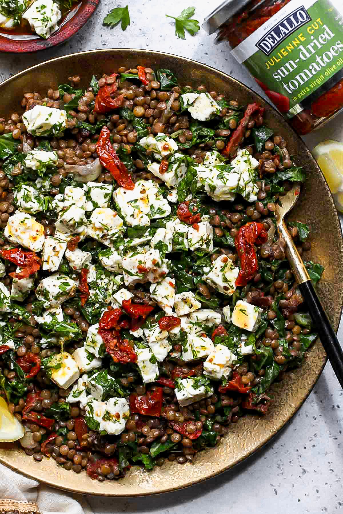 Warm lentil salad topped with marinated feta on a gold serving platter.