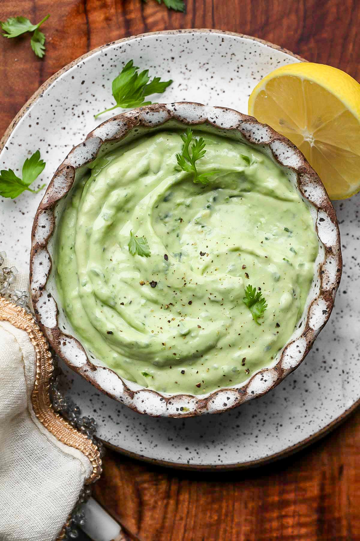 Avocado sauce in a small white scalloped bowl on a plate.