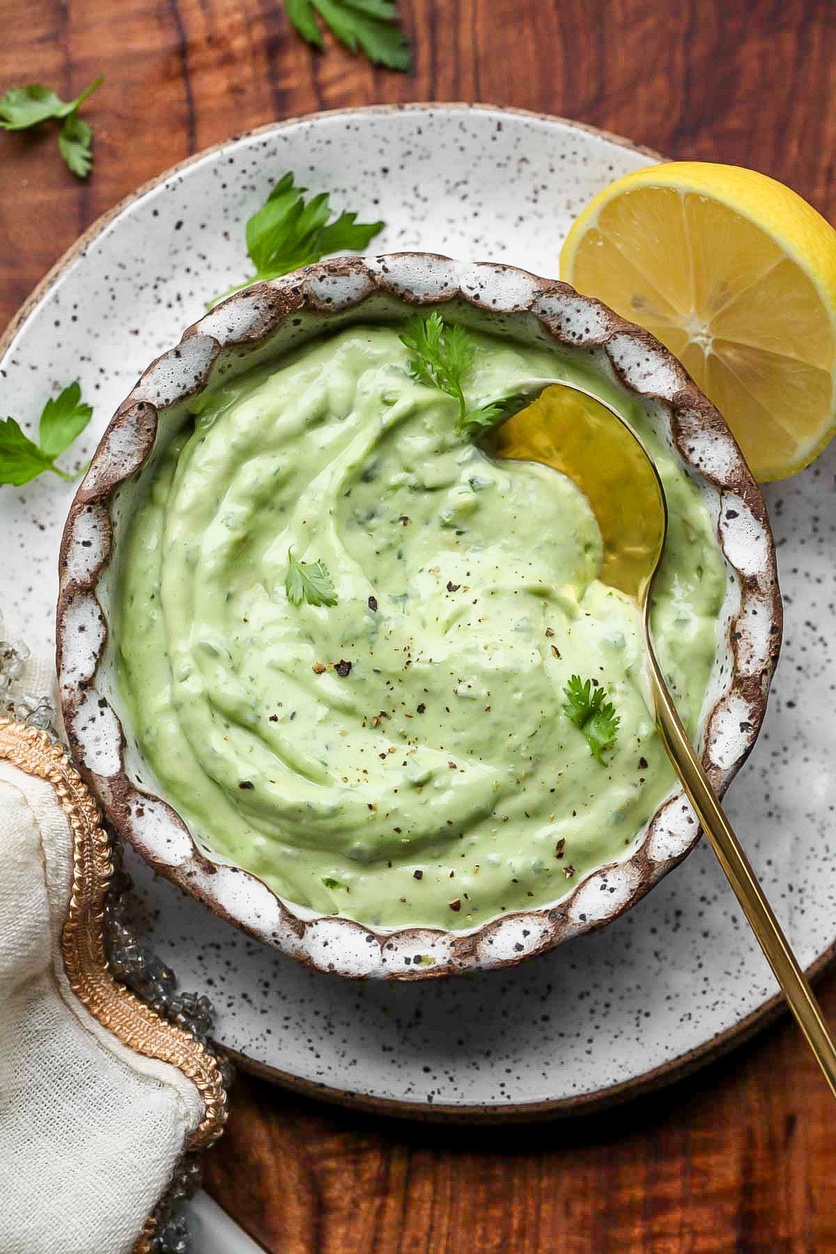 Avocado sauce recipe styled in a small white bowl with a golden spoon resting on the right side.