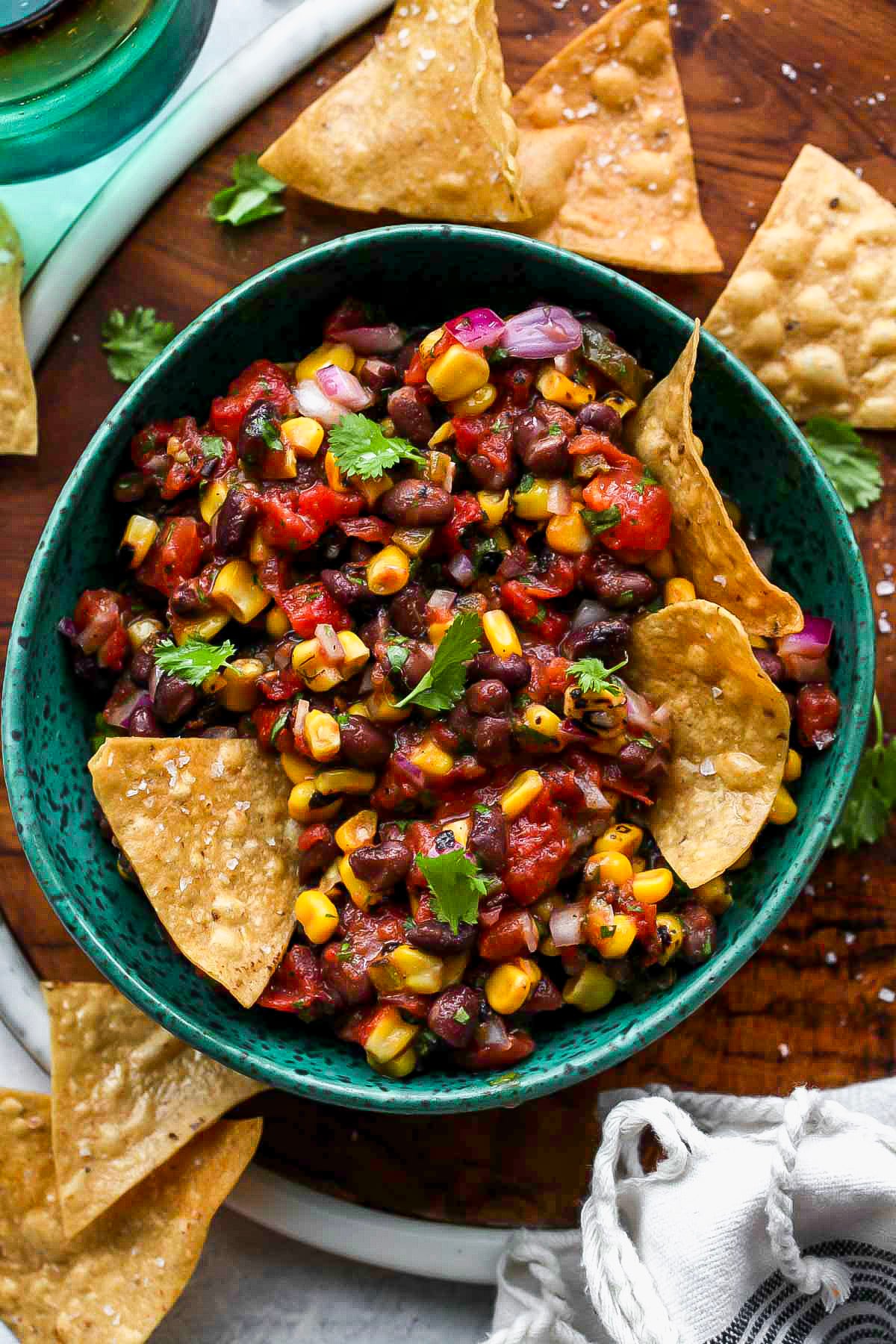 Zesty black bean salsa in a blue bowl with chips scattered around the bowl.