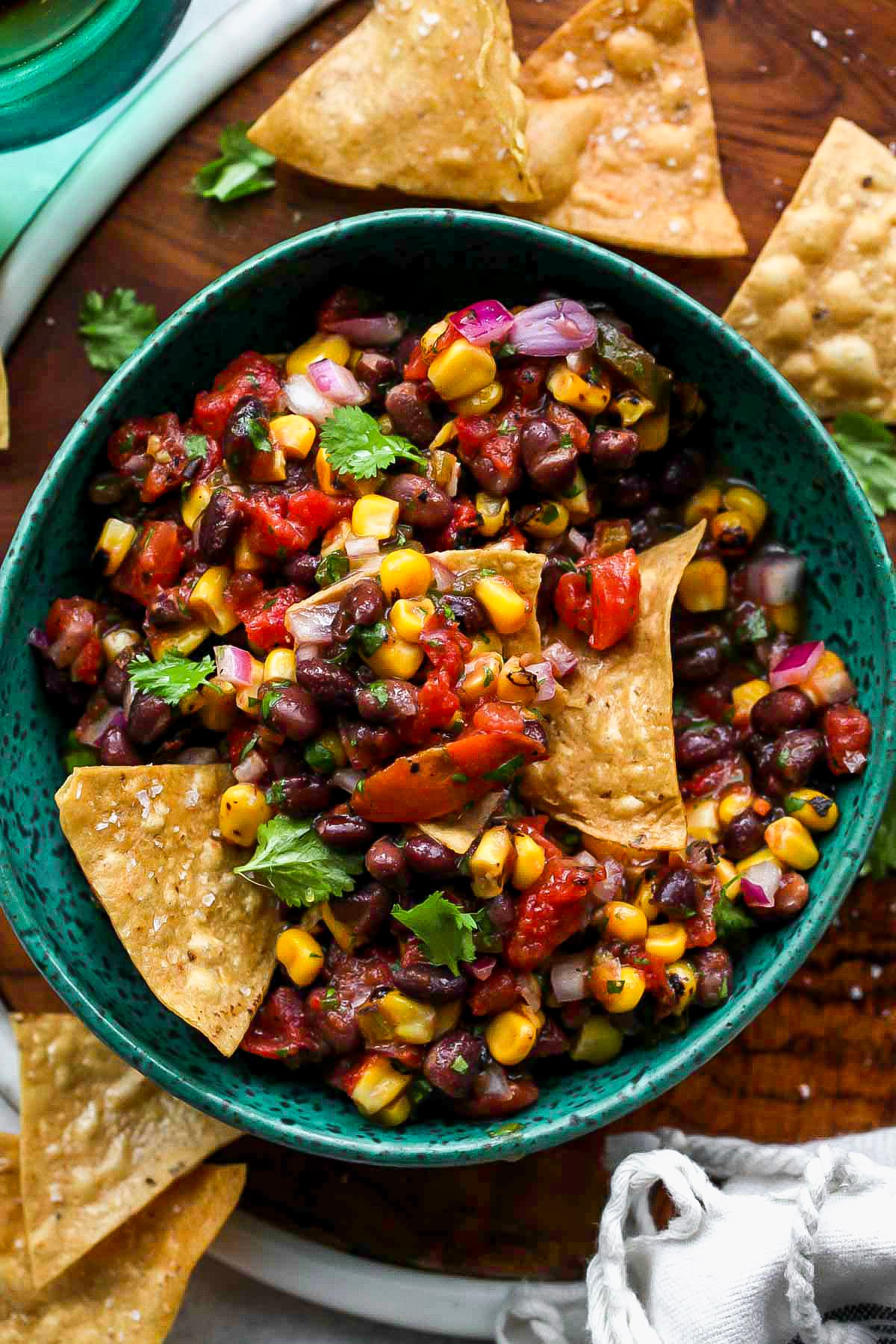Tortilla chips scooping up black bean salsa out of a blue bowl.