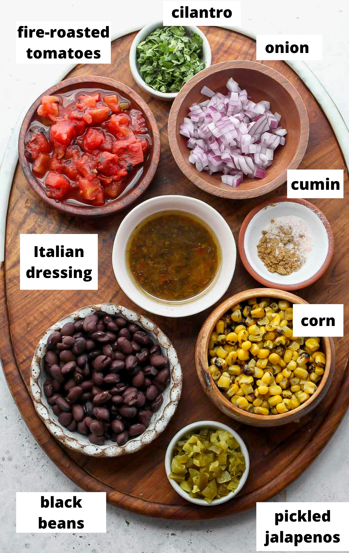 Recipe ingredients in separate bowls with labels on a wooden platter.