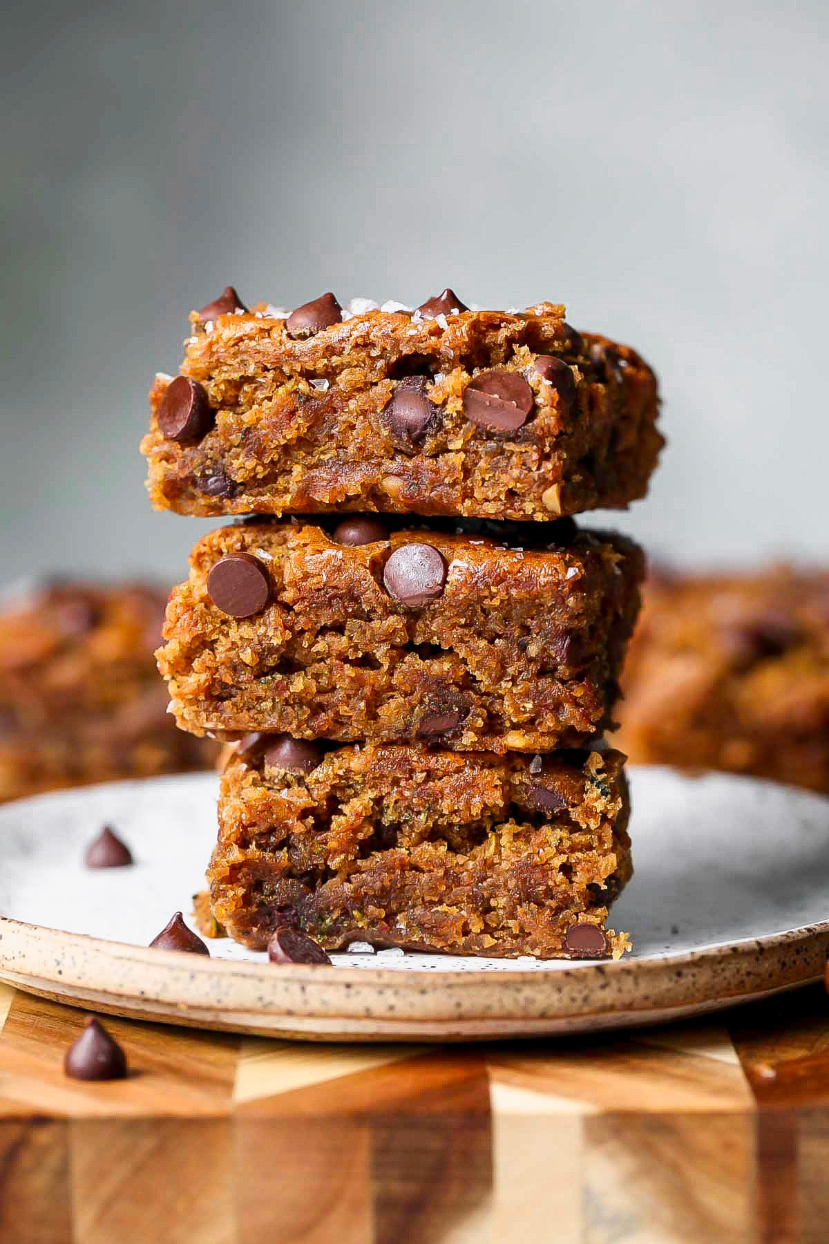 3 chocolate chip zucchini bars stacked on one another on a white plate.