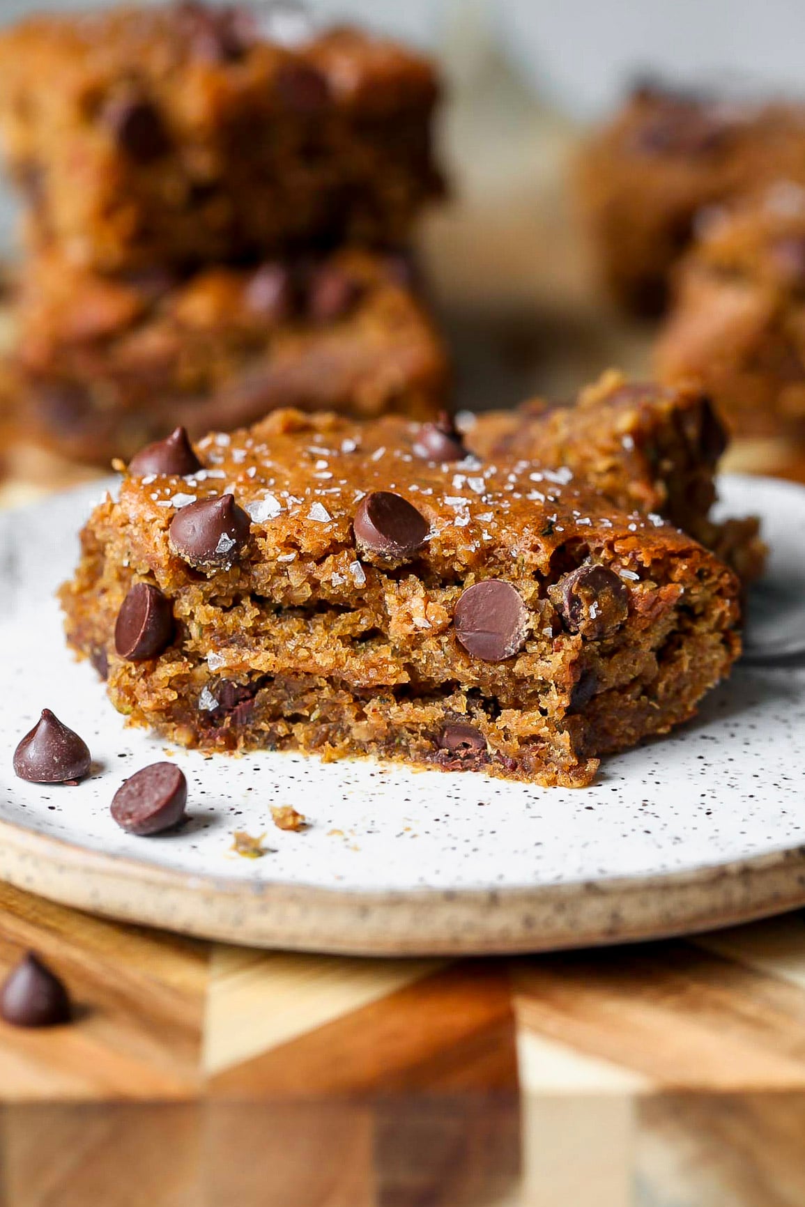 A chocolate chip zucchini bar on a small white plate with a bite removed to show inside texture.