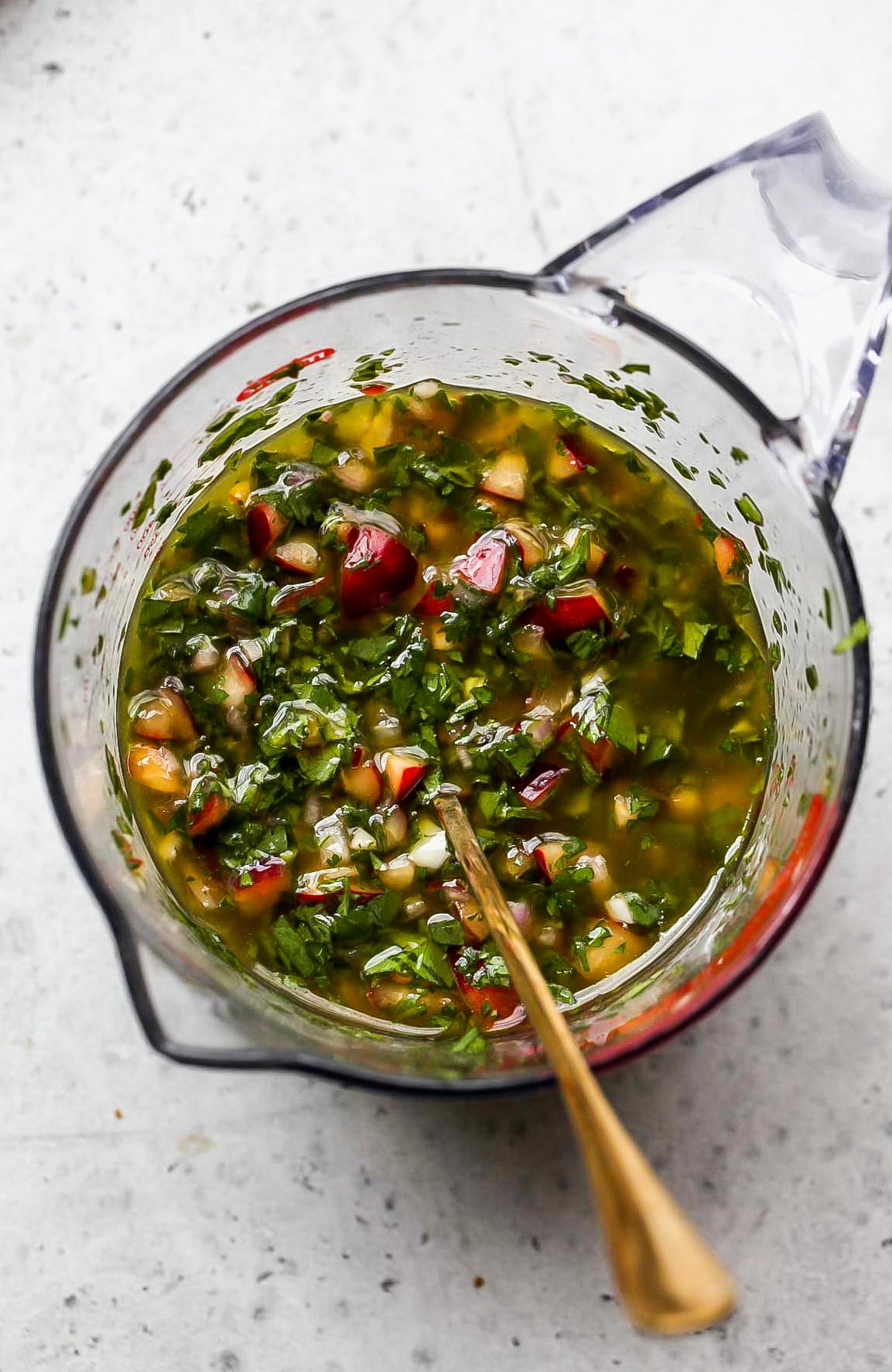 Ingredients being added to a clear glass measuring cup and mixed to combine.