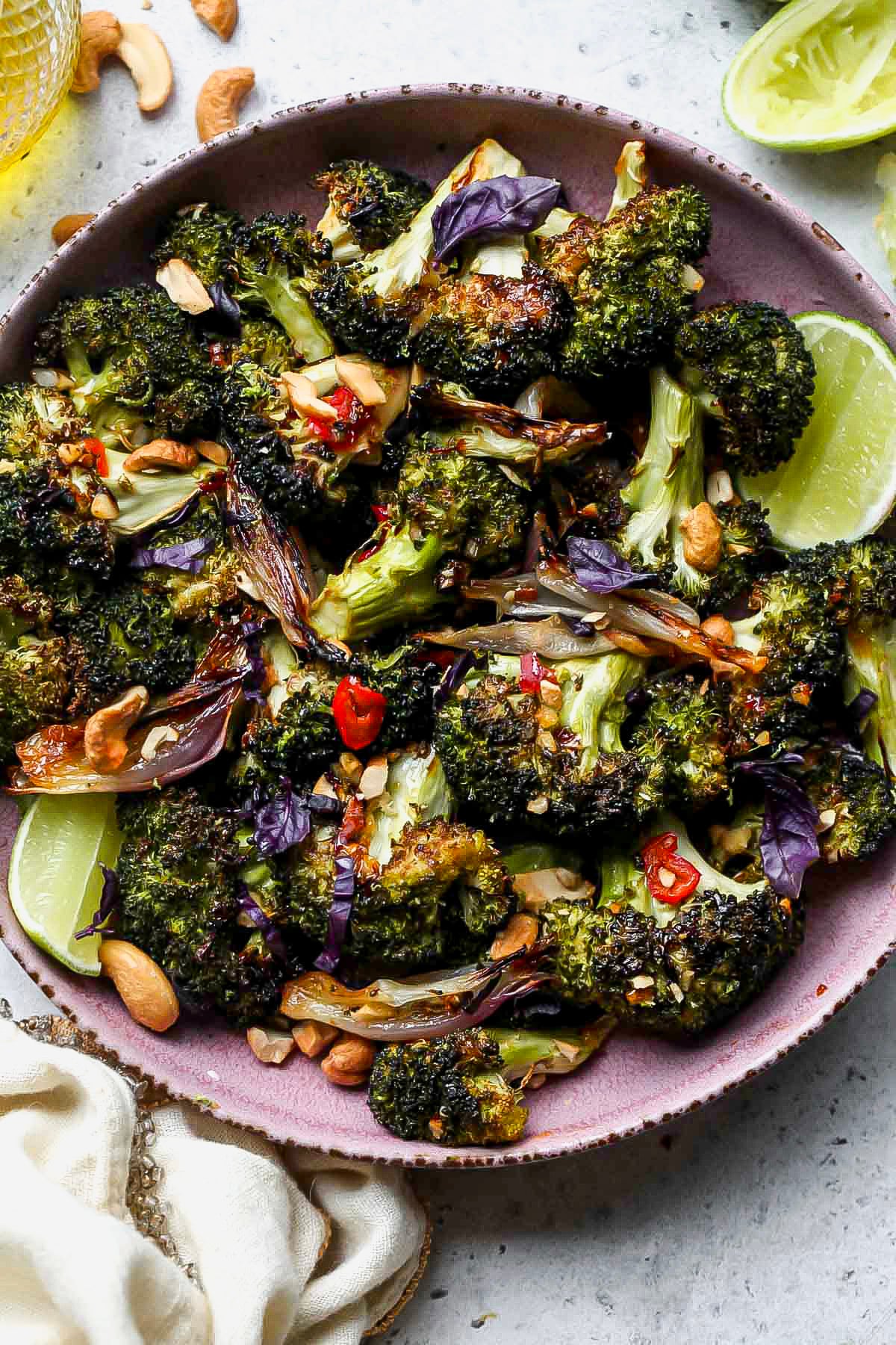 Roasted broccoli with chili-garlic sauce in a pink serving plate topped with roasted cashews.