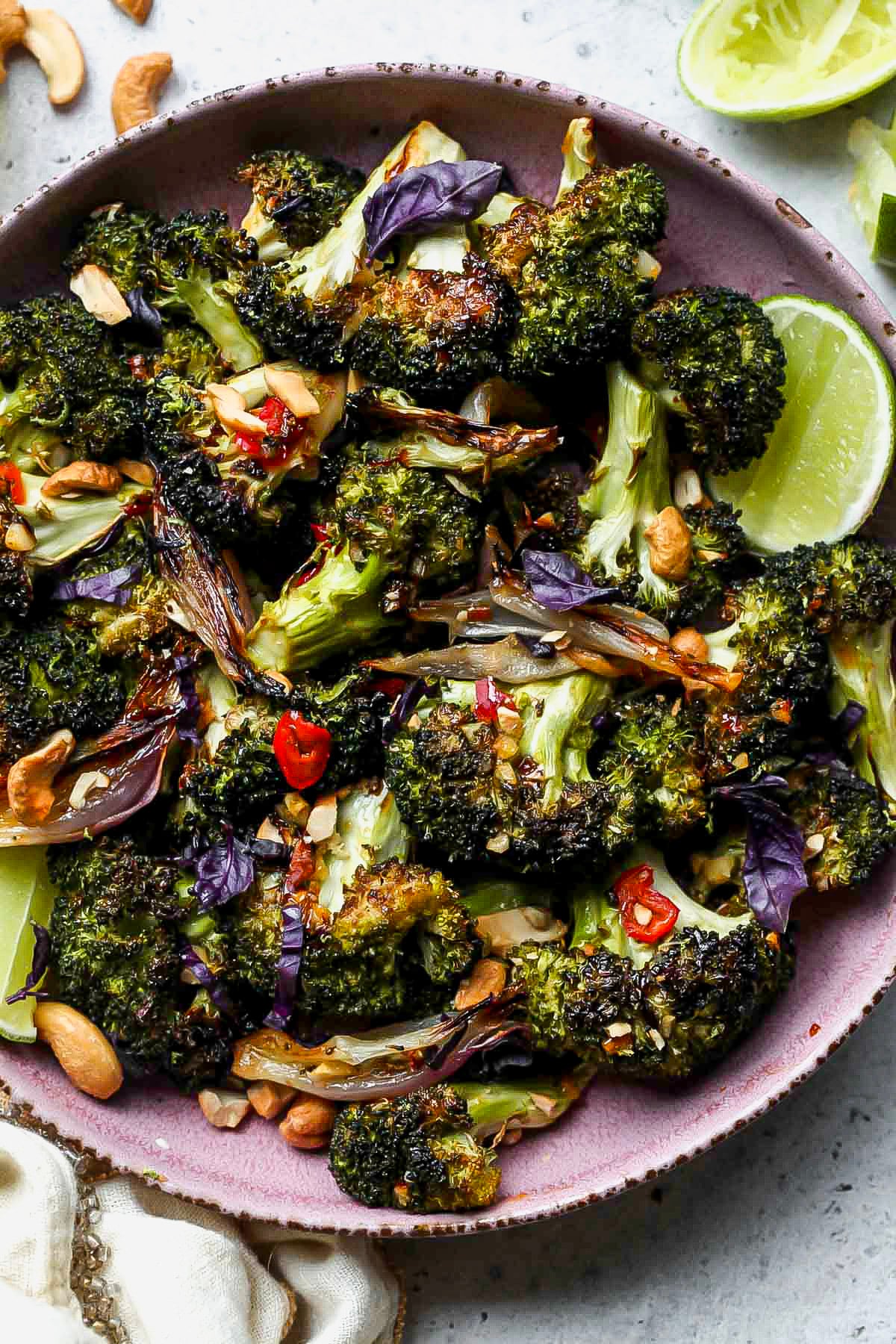 Roasted broccoli recipe topped with chili-garlic sauce, lime, and cashews in a pink bowl.
