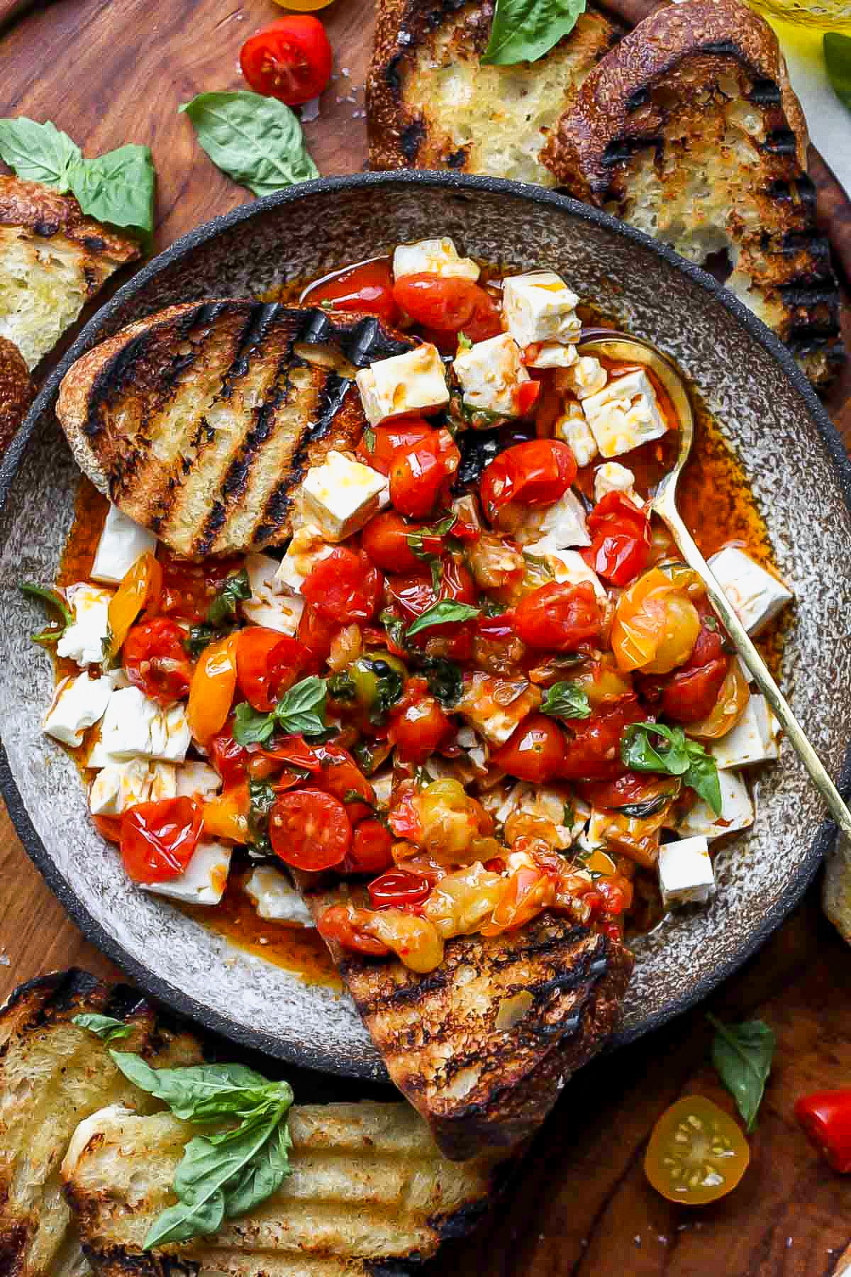 Grilled bread being dipped into a bowl of spicy tomato marinated feta.
