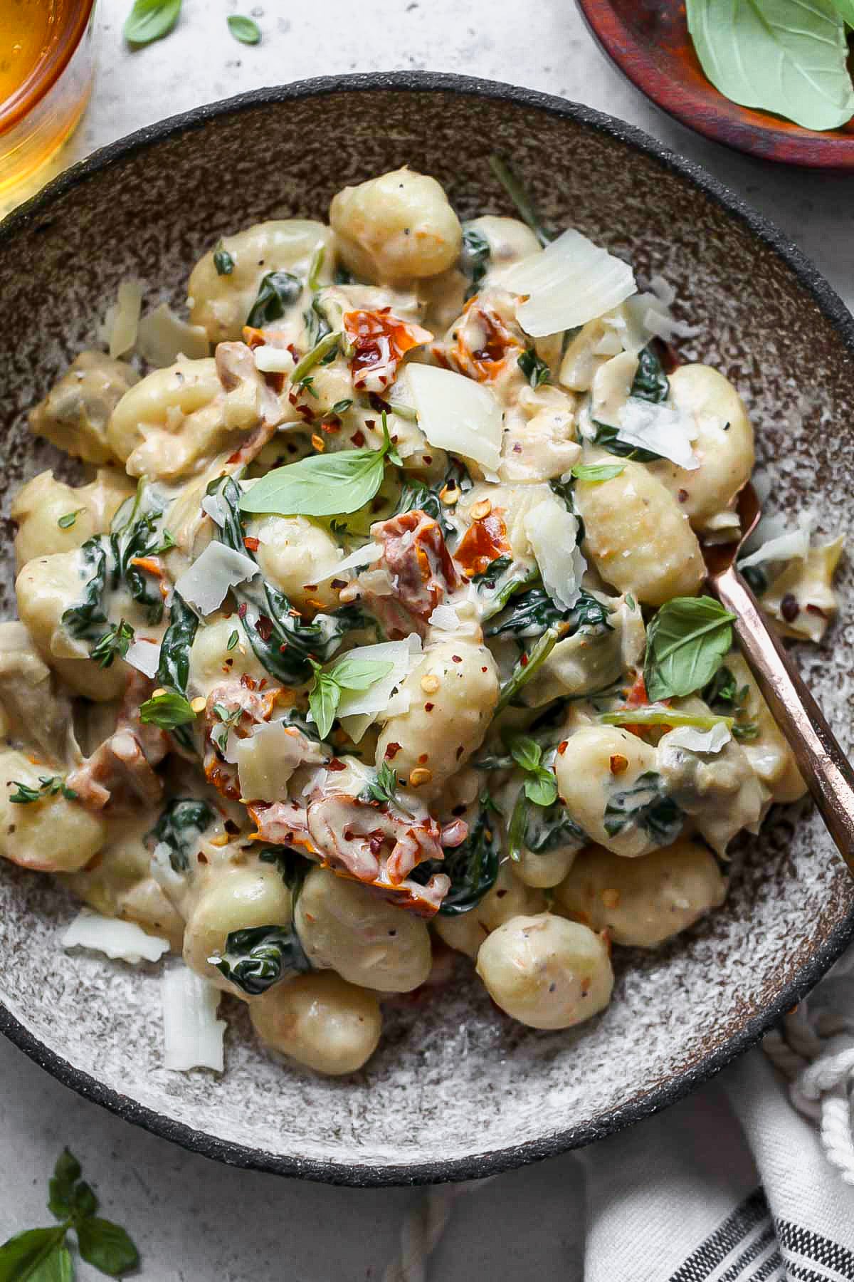Creamy sun-dried tomato gnocchi recipe topped with Parmesan in a grey bowl.