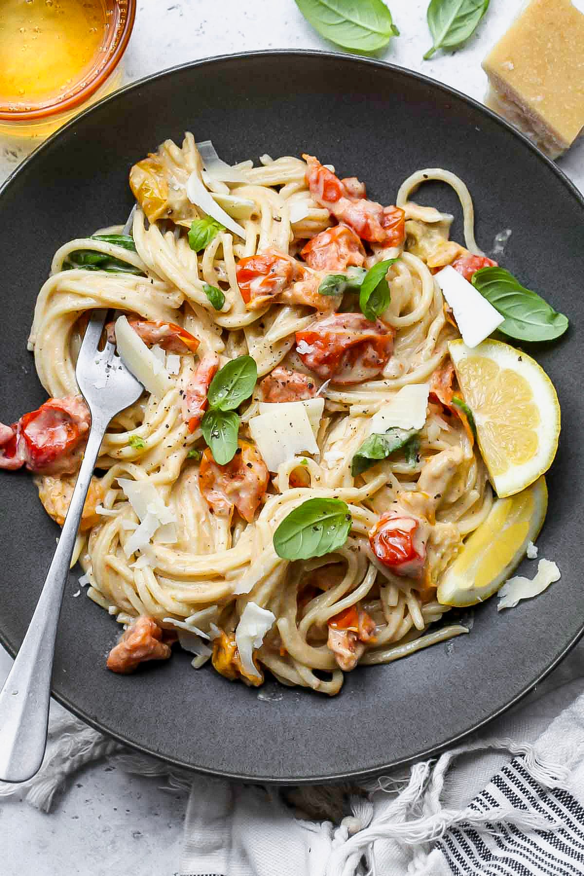 Tahini Pasta with burst tomatoes and parmesan in a grey serving bowl with a fork resting on the side.
